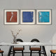 A modern dining area features a marble table, four chairs, and a glass vase with white flowers. Above, three Trevasse Aqua Blue Textured Abstract Framed Wall Art pieces by Giant Sculptures add vibrant color to the light gray wall.
