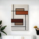 The Gridoria Rust & Taupe Linear Block Woven Wall Art by Giant Sculptures features black lines and rectangles in rust, orange, and beige shades—perfect for modern minimalist decor above a white cabinet with a plant and gold accent.