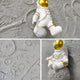 The Astravera Lunar Crew Grey Textured Astronaut 3D Wall Art by Giant Sculptures features a small astronaut with a gold helmet on a moon-like surface—ideal as unique children's room decor or eye-catching wall art.