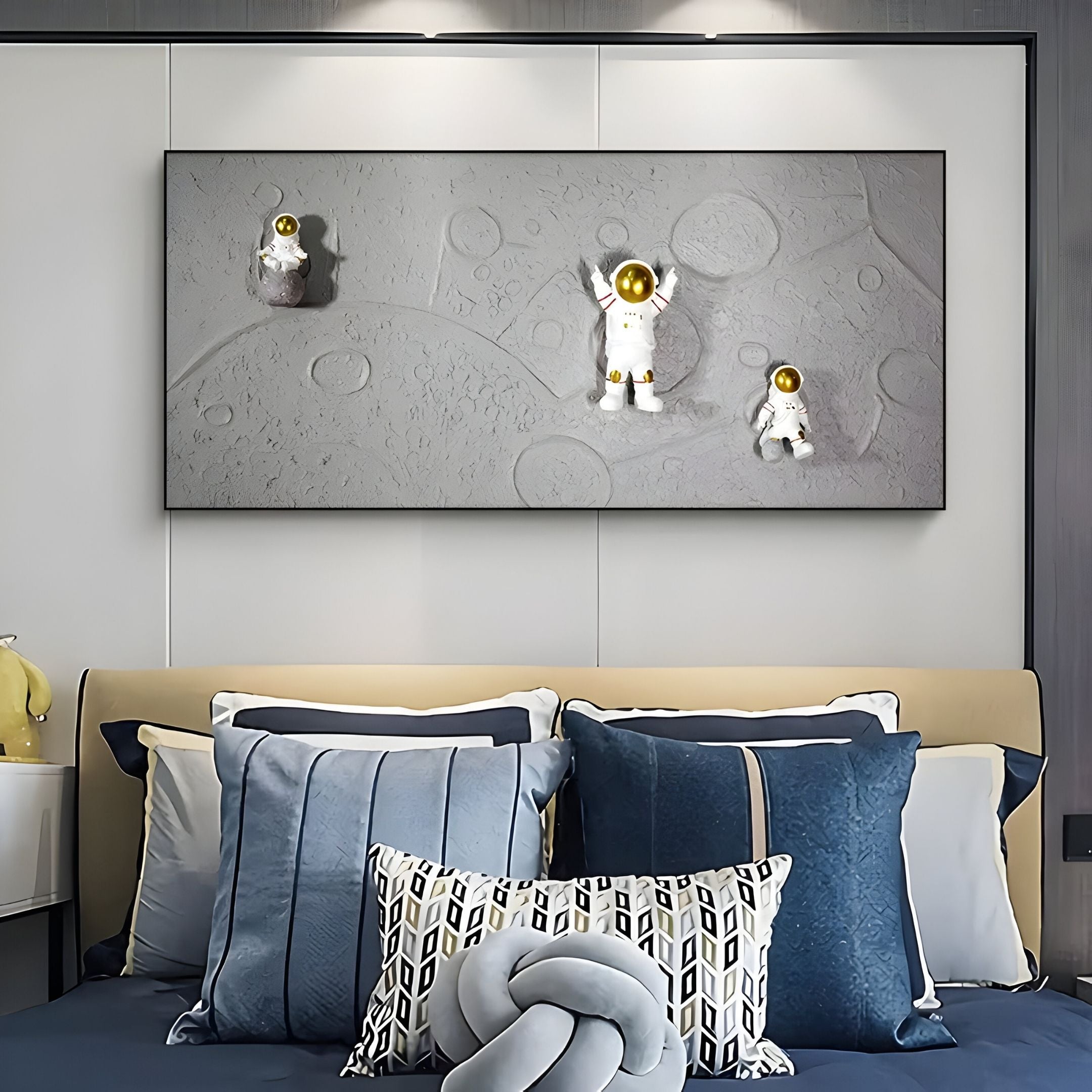 A modern bedroom with blue and gray pillows on the bed, highlighted by Giant Sculptures' Astravera Lunar Crew Grey Textured Astronaut 3D Wall Art above—an inspiring option for children's wall decor.