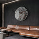 A modern living room with a brown leather sectional sofa, round coffee table, and the Lumineris Silver Ripple Sphere Metal 3D Wall Art by Giant Sculptures mounted on a dark gray textured wall.