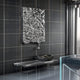 A modern interior with dark plaid tile walls showcases the Lumineris Silver Drip Cascade Metal 3D Wall Art by Giant Sculptures above a sleek black marble bench topped with a coiled black accent, alongside glass and steel elements.