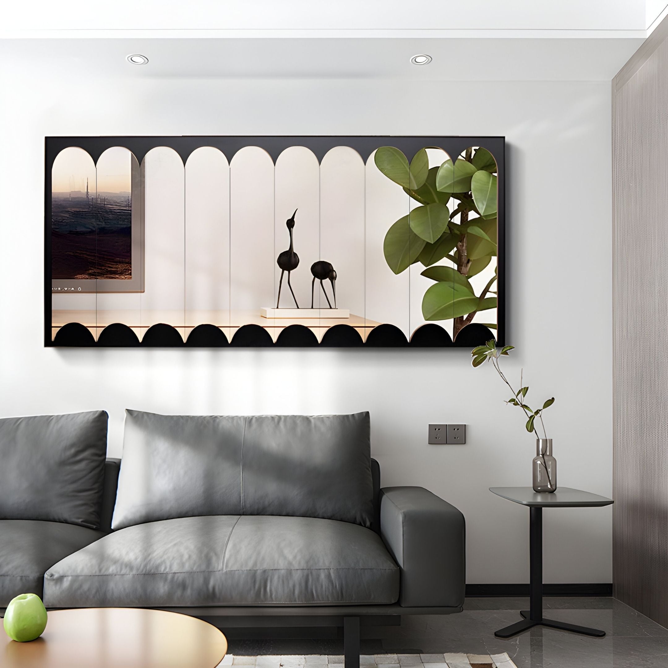 A modern living room features a gray sofa, a small side table with a plant, and the Lumiscale Black & Taupe Modular Glass Wall Mirror by Giant Sculptures, reflecting two black bird figurines and part of a leafy plant.
