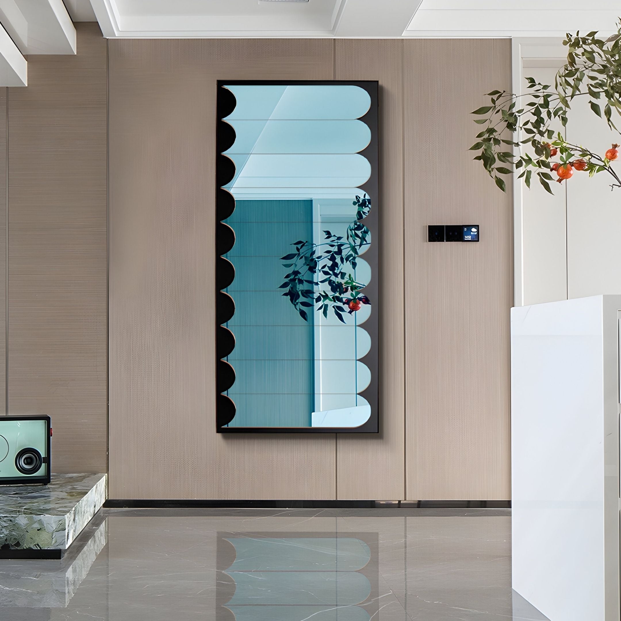 A modern interior showcases the Lumiscale Black & Blue Modular Glass Wall Mirror by Giant Sculptures on a beige wall, reflecting a branch with orange-red flowers, as marble flooring and a sleek white counter enhance the space's brightness.