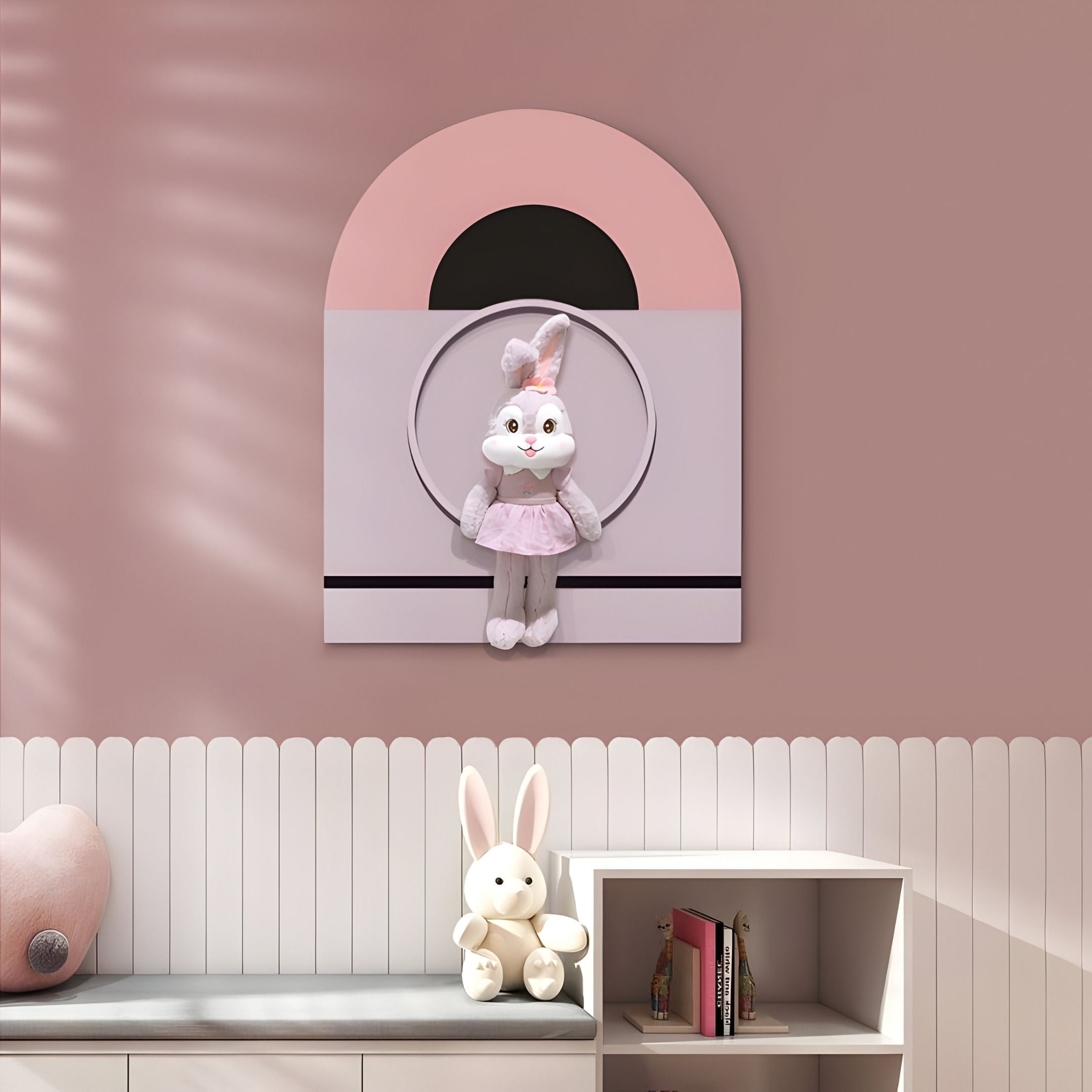 The Cuddiloft Pink Bunny Plush Display 3D Wall Art by Giant Sculptures hangs above a white shelf with another bunny doll and books, making charming nursery wall decor against a pink and white paneled wall.