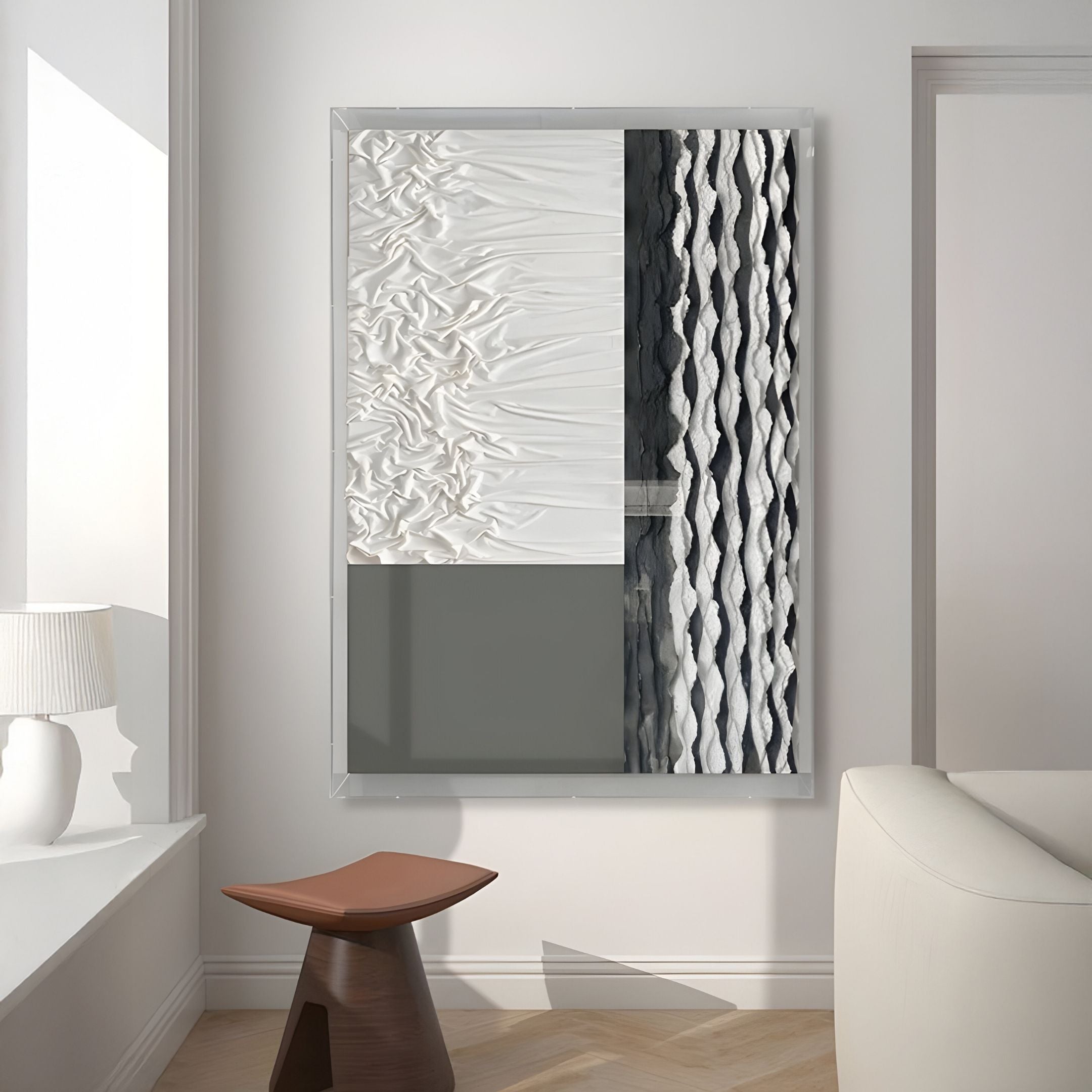 The Texturien White & Slate Grey Paper Abstract 3D Wall Art by Giant Sculptures hangs above a brown angular stool in a minimalist room with white walls, curved sofa, and lamp—perfect for contemporary interiors.