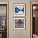 The Stratum Blue Crest Textured Abstract Framed Wall Art by Giant Sculptures, featuring bold blue shapes on beige, is displayed in black frames, one above the other, on a light wall in a modern hallway.