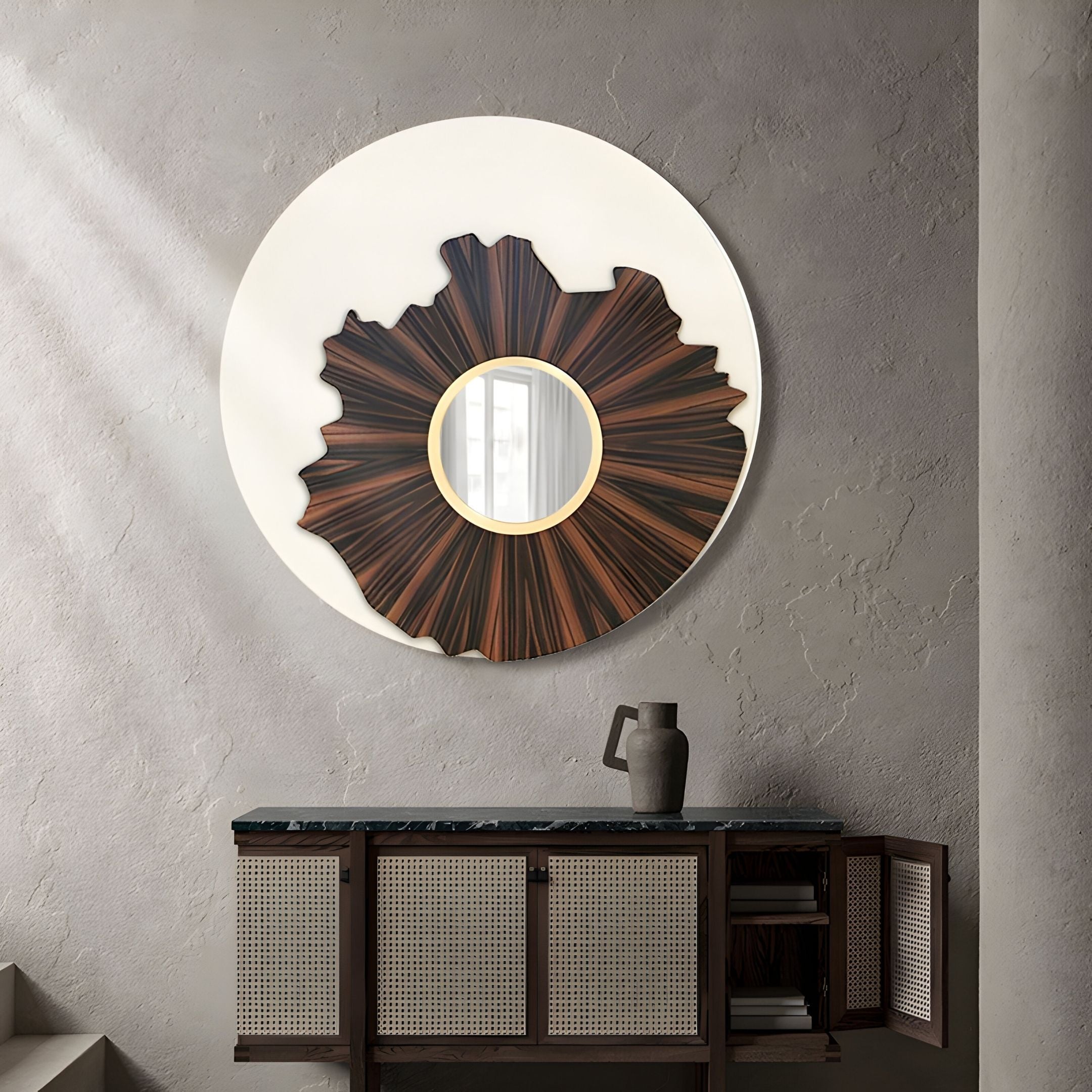 The Lunestre Walnut Burst Round Sculptural Mirror 3D Wall Art by Giant Sculptures hangs on a textured beige wall above a cabinet with rattan doors. A ceramic pitcher sits nearby and one cabinet door is open, adding depth and interest to the space.
