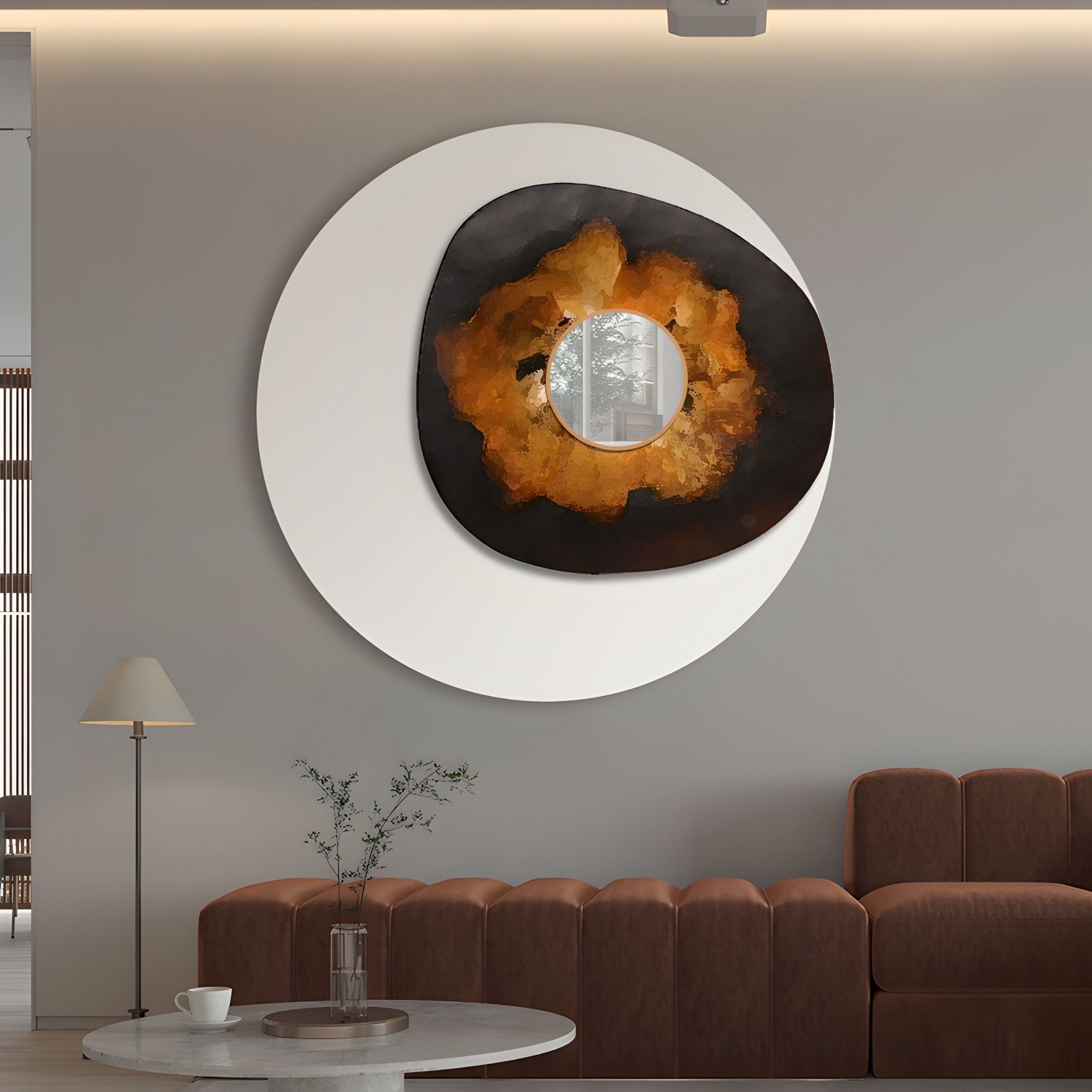A modern living room with a brown sofa, marble coffee table, and the Giant Sculptures Lunestre Ember Bloom Abstract Round Mirror 3D Wall Art featuring black and gold shapes on white. A lamp and small plant add to the minimalist decor.