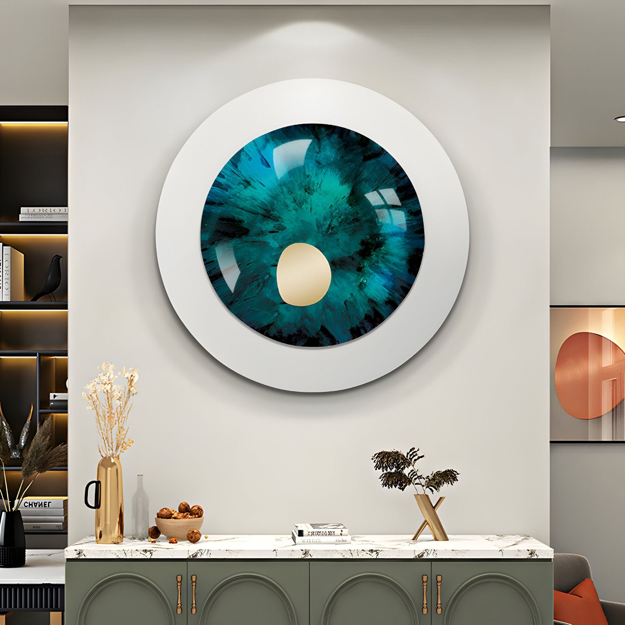 The Iriselle Emerald Crystal Porcelain Round 3D Wall Art by Giant Sculptures, resembling a blue-green eye with a gold center, hangs above a white countertop adorned with vases, dried flowers, and snacks in this modern room.