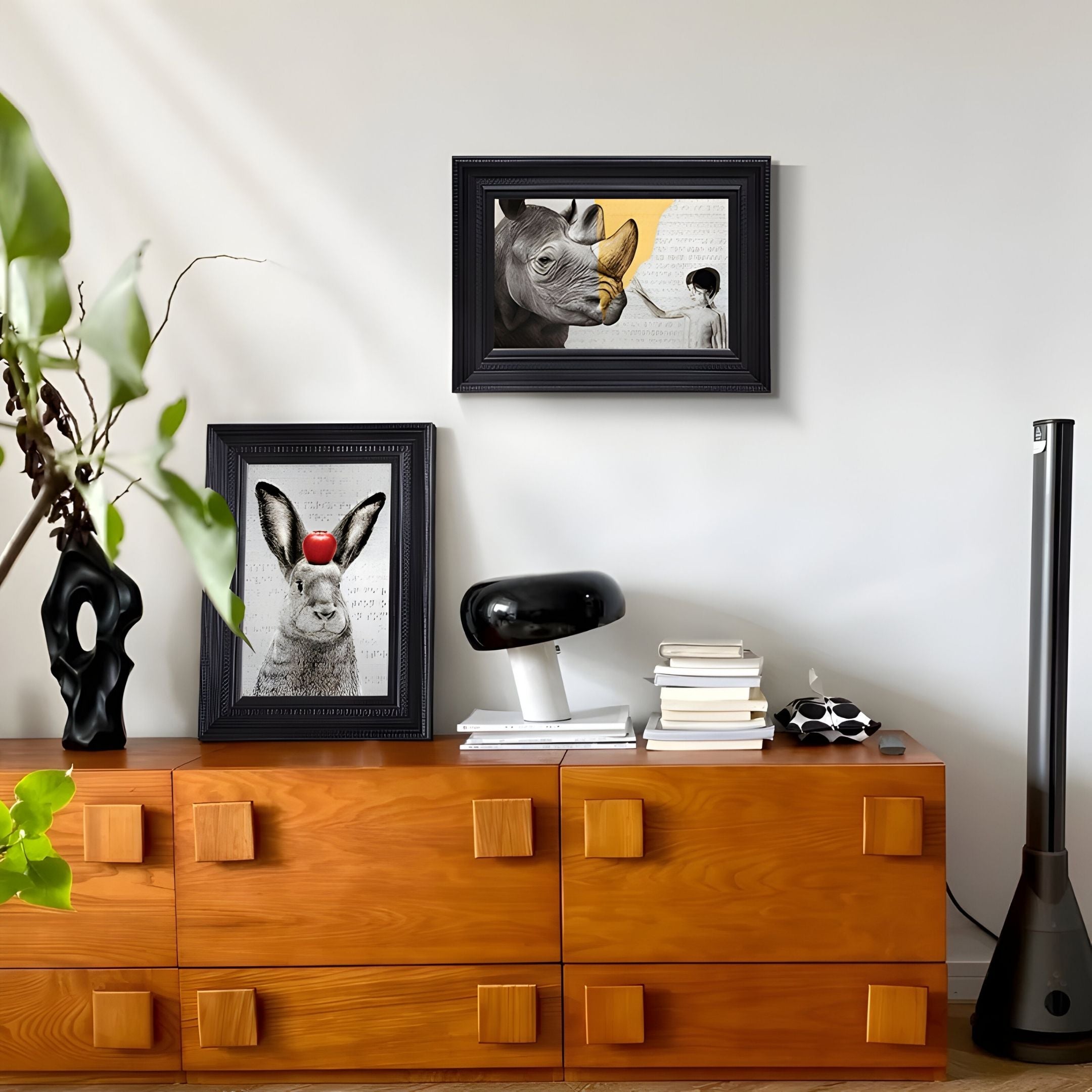 A modern wooden sideboard displays books, a black abstract sculpture, and a lamp beneath the Giant Sculptures Ardensir Rabbit & Rhino Surreal 2-Set Framed Wall Art on a light-colored wall.