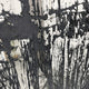 The Rivarenne Black Abstract Texture Steel Mirror 3D Wall Art by Giant Sculptures features vertical streaks inspired by dripping paint or ink on glass, creating a bold, uneven pattern that stands out against a blurred light background.
