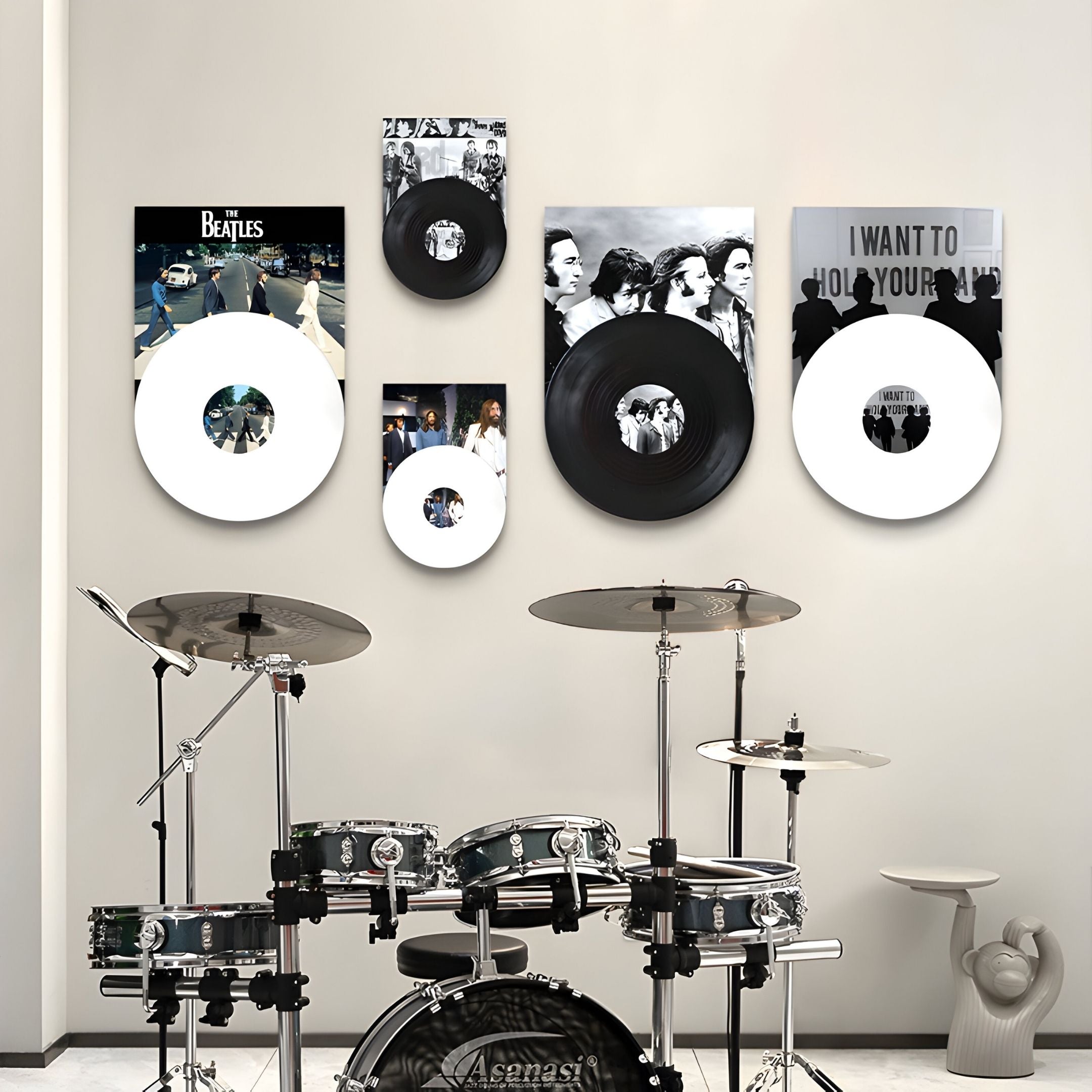 A modern music room features a drum set before a beige wall, decorated with Giant Sculptures' Pressline Beatles Classics Record Collage 5-Panel Wall Art and vinyl records. To the right, a unique white hand-shaped chair adds flair.