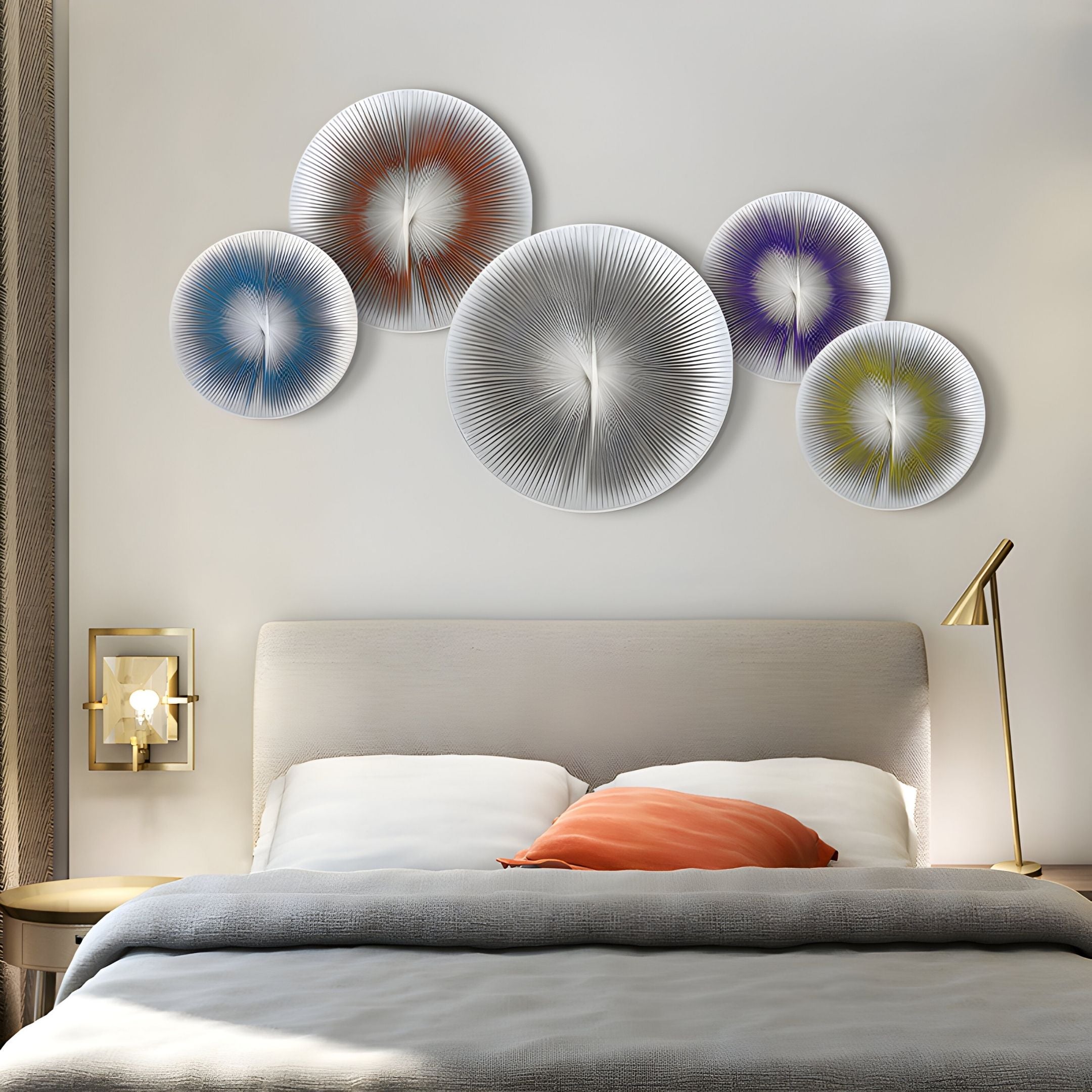 A modern bedroom features a beige upholstered bed with white and gray bedding, an orange pillow, and the Centria III Multicolour Disc 5-Panel 3D Leather Wall Art by Giant Sculptures above the bed. Gold lamps adorn the nightstands.