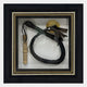 The CurioVault Braided Leather Loop & Medallion Framed Wall Art by Giant Sculptures showcases a black braided leather loop, rolled sheet music, and a gold medallion on white with a black and gold border.