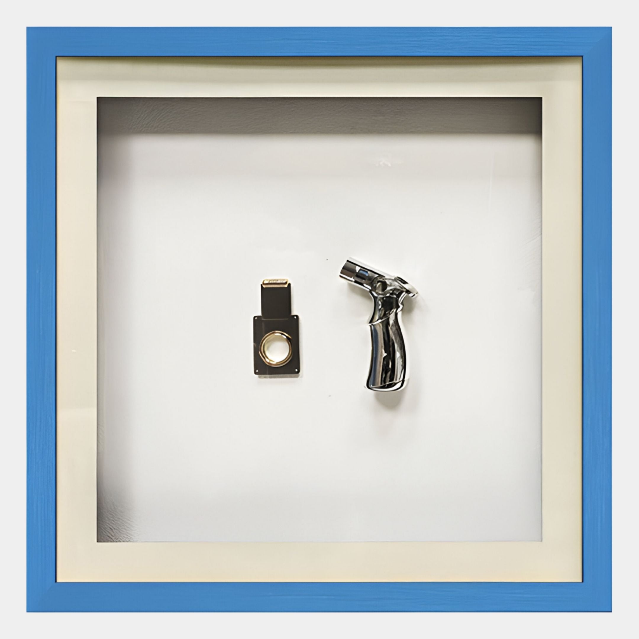 The Valet Noir Cigar Cutter & Torch Blue Framed Wall Art by Giant Sculptures features a contemporary still life with two metallic objects—a cigar cutter and a torch—displayed on a white background with a blue border.