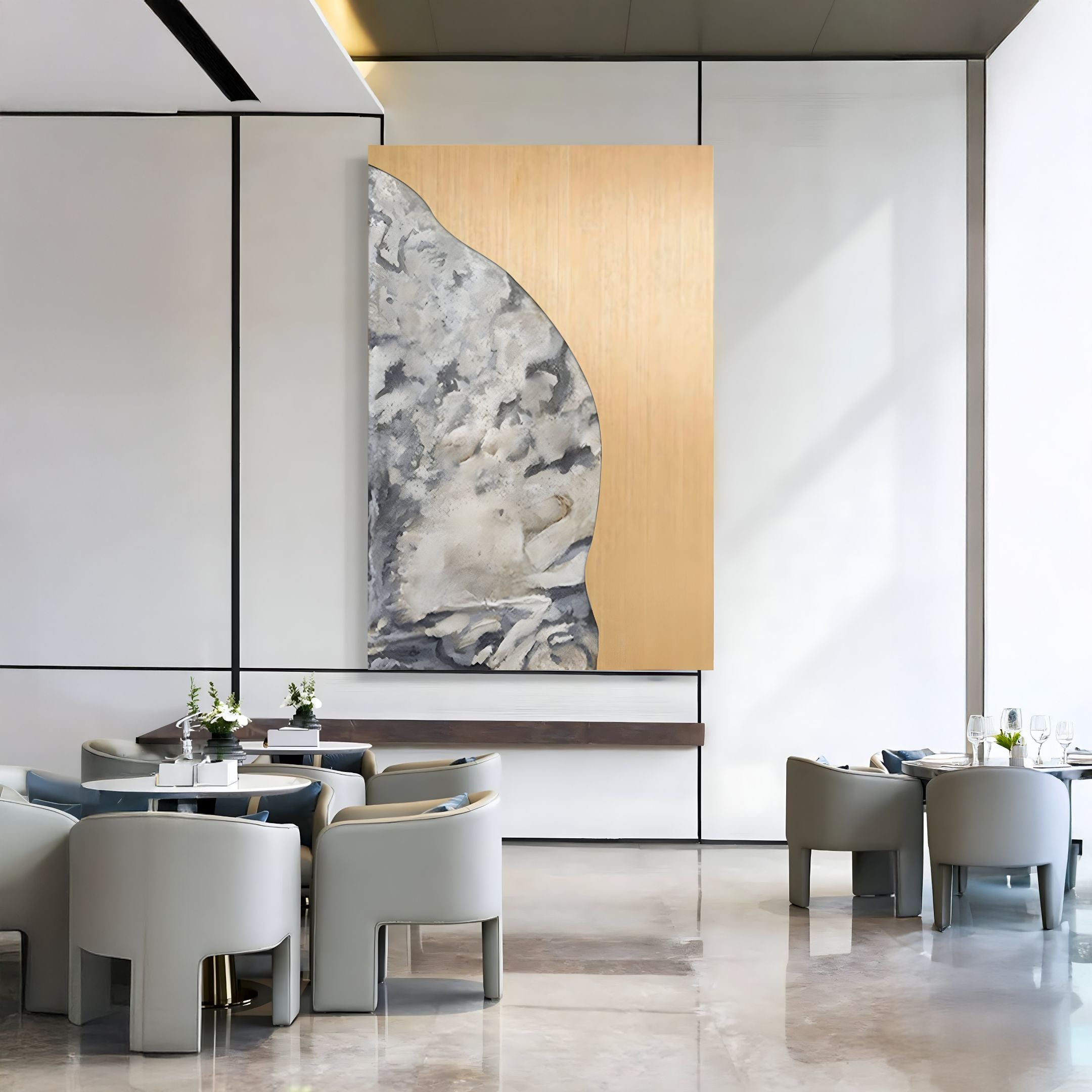 A modern dining area features gray armchairs around round tables, white walls, and Giant Sculptures’ Gildrift Gold Steel & Stone Grey Curve Textured 3D Wall Art. The polished floor reflects the furniture, highlighting the contemporary decor.