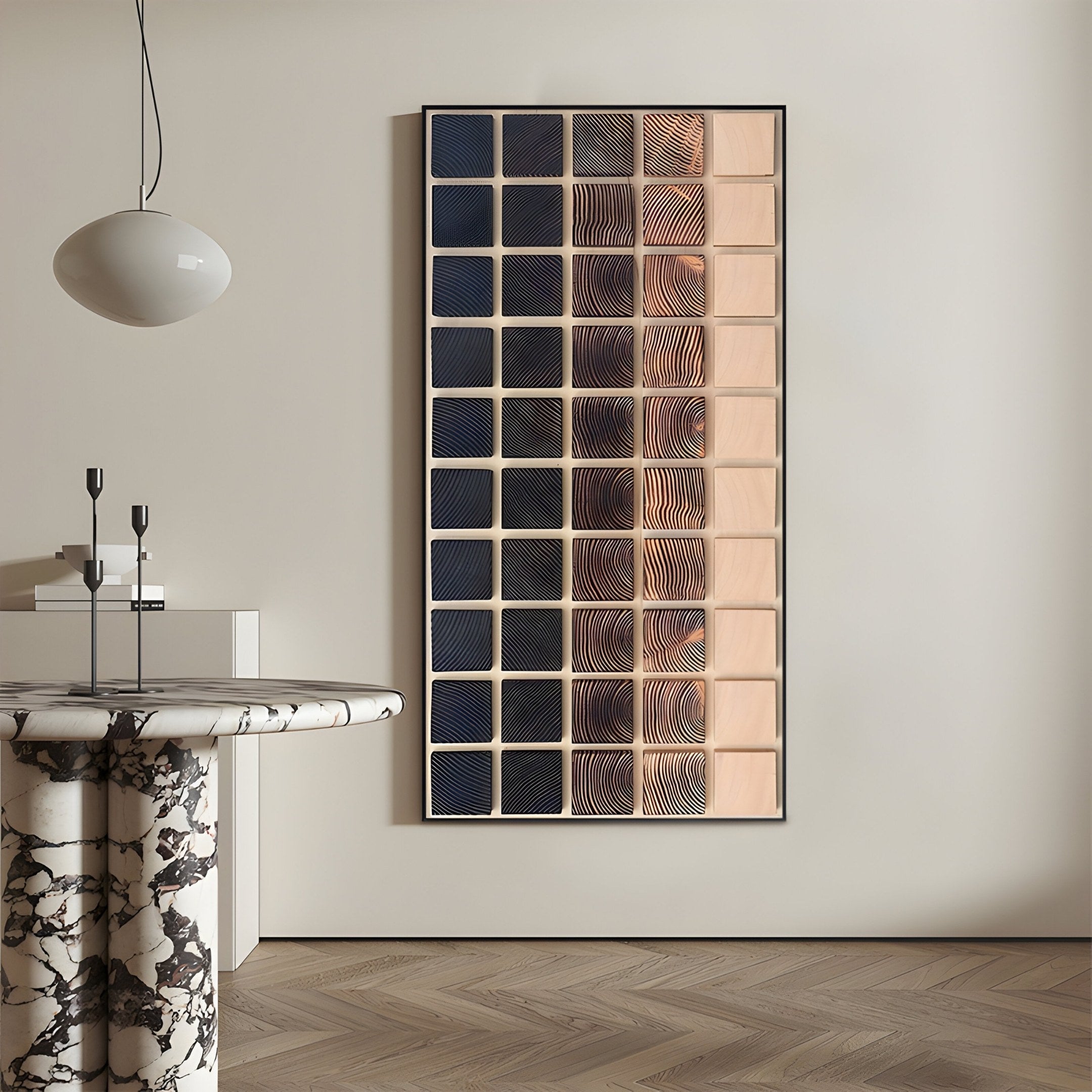 A modern interior featuring a round marble table, two black candle holders, and the Quadrelle Midnight & Sand Grid Geometric 3D Wall Art by Giant Sculptures displayed above herringbone wood flooring on a beige wall.