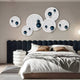 A modern bedroom with a dark upholstered headboard, neatly made white and beige bed, round side tables, and the Orbiora Blue Orb 5-Panel Concentric Sphere 3D Wall Art by Giant Sculptures as a striking focal point above the bed.