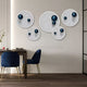 A modern dining area features navy velvet chairs, a wooden table, and Giant Sculptures' Orbiora Blue Orb 5-Panel Concentric Sphere 3D Wall Art. Light from the left highlights the glossy blue sphere design and enhances the contemporary decor.