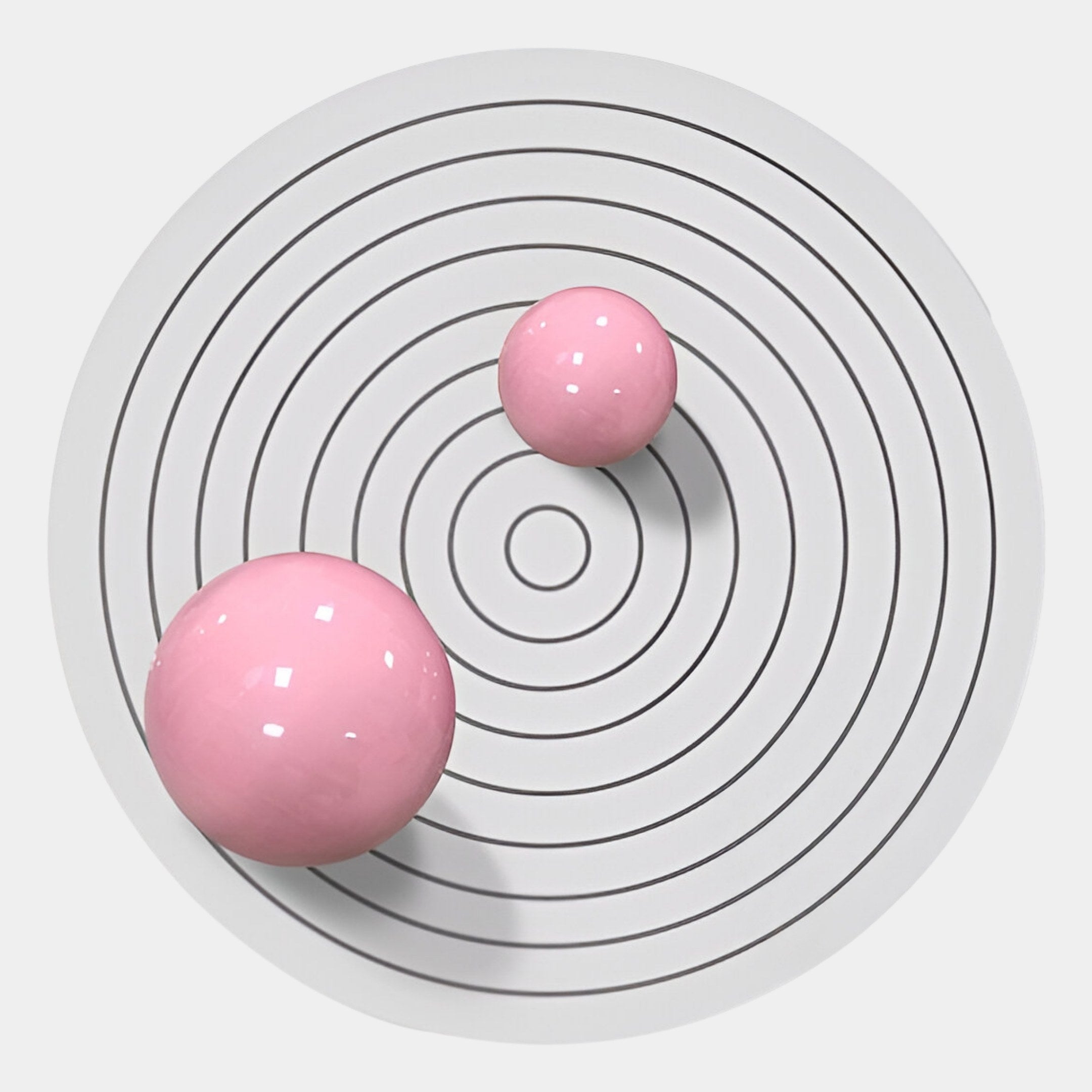 The Orbiora III Pink Duo Concentric Sphere 3D Wall Art by Giant Sculptures features two glossy pink spheres of varying sizes on a white surface with black concentric circles, bringing minimalistic yet bold modern style to your space.