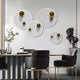 A modern dining room with a round table, gray and gold chairs, a plant centerpiece, a black sculpted bust on a pedestal, and Giant Sculptures’ Orbiora Gold Orb 4-Panel Concentric Sphere 3D Wall Art as an eye-catching feature.