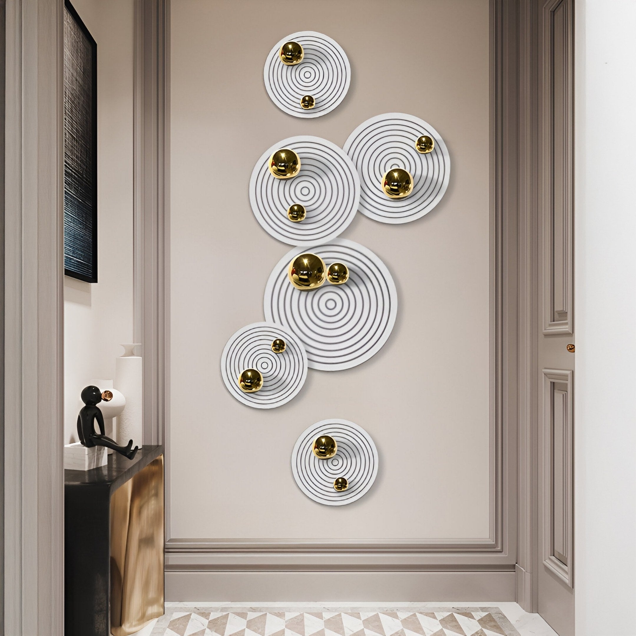 A beige hallway showcases the Orbiora Gold Orb 6-Panel II Concentric Sphere 3D Wall Art by Giant Sculptures, featuring reflective gold spheres. The geometric patterned floor and a small black figurine add to the modern sculptural style.