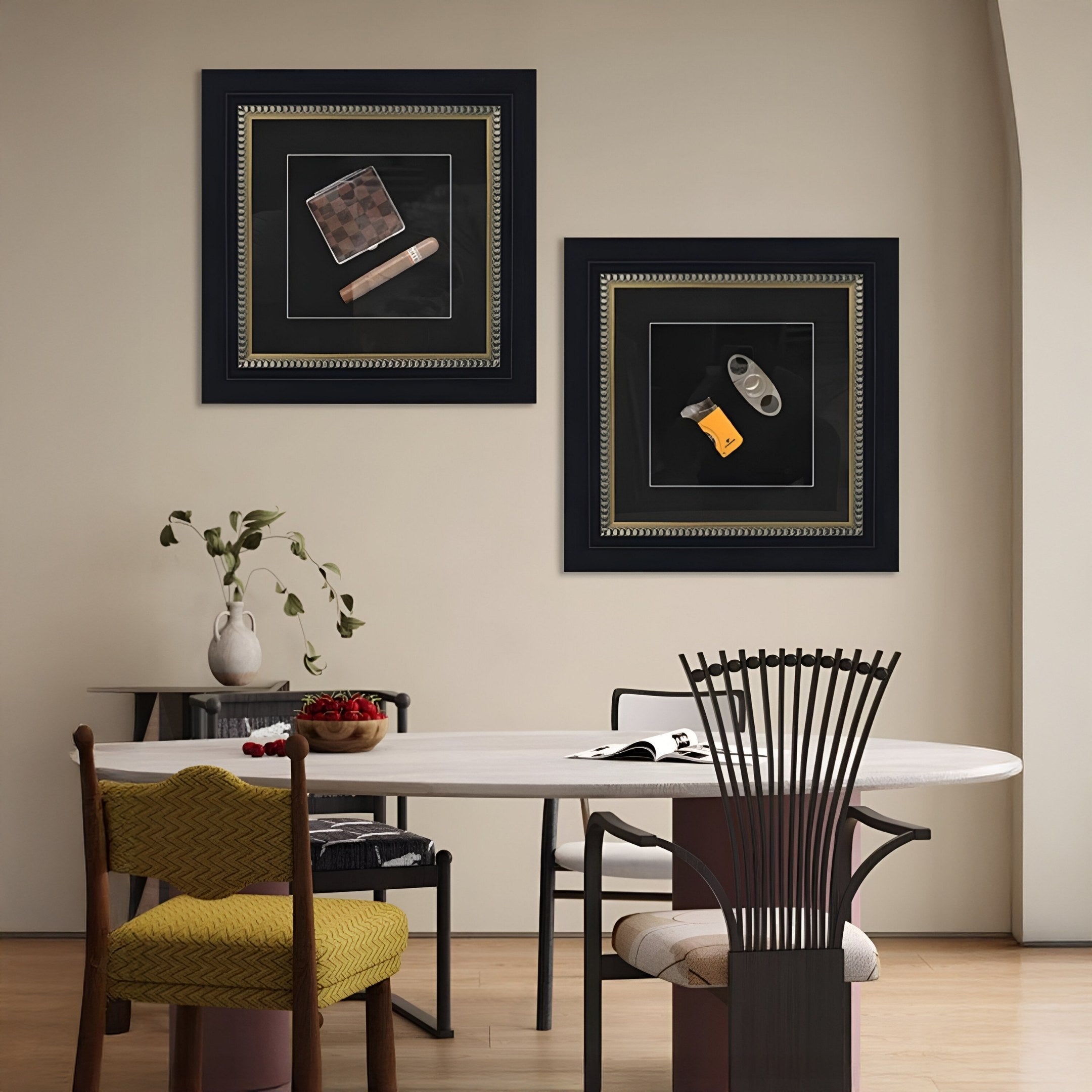 A modern dining area features a round white table, four chairs, and a vase with branches. Two Havantra Cigar & Checked Case Framed Wall Art pieces by Giant Sculptures hang on the beige wall above the table.