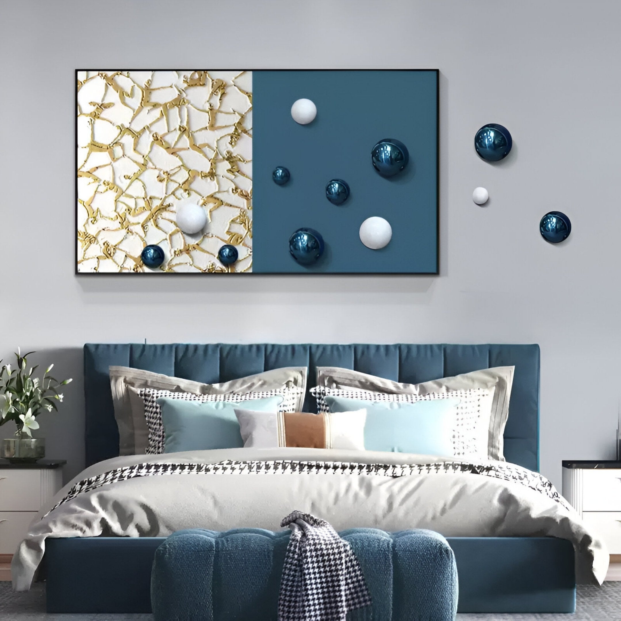 A modern bedroom features a blue upholstered bed with patterned pillows and throws. Above the bed hangs Giant Sculptures' Spherium Blue & White Orb Dual-Tone Panel 3D Wall Art, accented with gold, white, and blue decorative spheres.