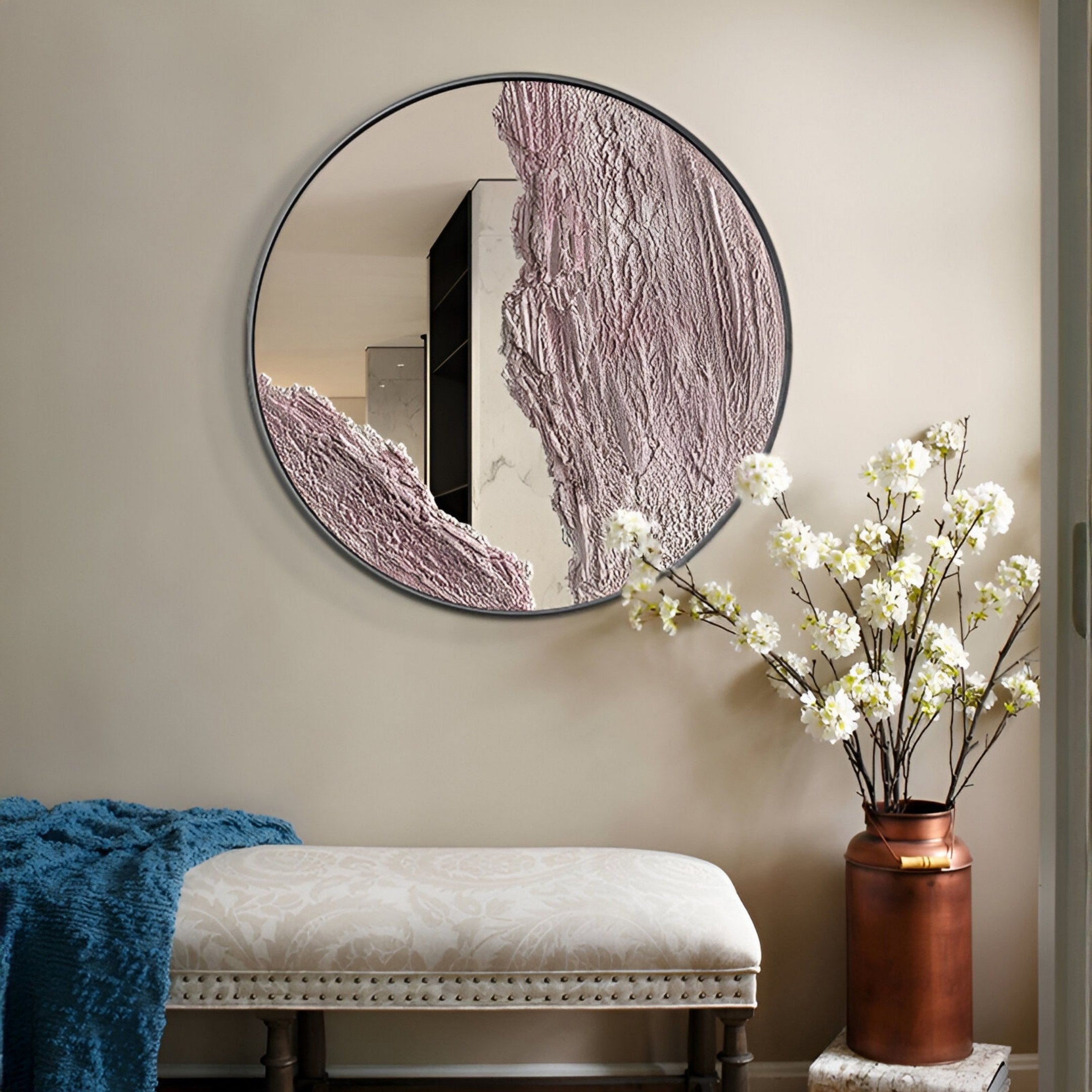 The Erosian Blush Vein Textured Round Mirror 3D Wall Art by Giant Sculptures hangs above an upholstered bench. A tall copper vase with white flowering branches stands nearby, while a blue throw adds a pop of color to the neutral space.