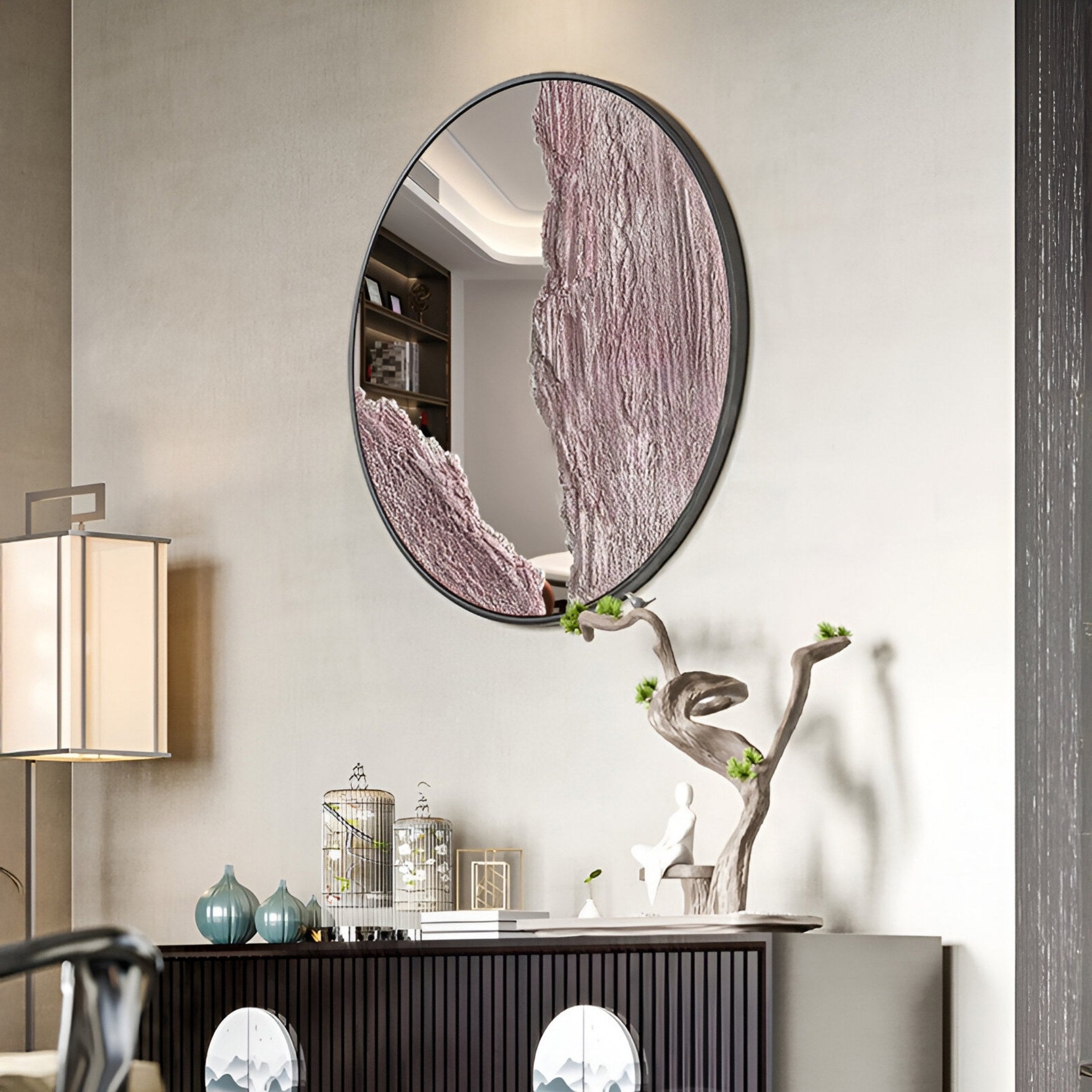 The Erosian Blush Vein Textured Round Mirror 3D Wall Art by Giant Sculptures features a pink and silver lower-right design, mounted above a dark console with sculpture and branch décor, complementing the neutral wall and modern style.
