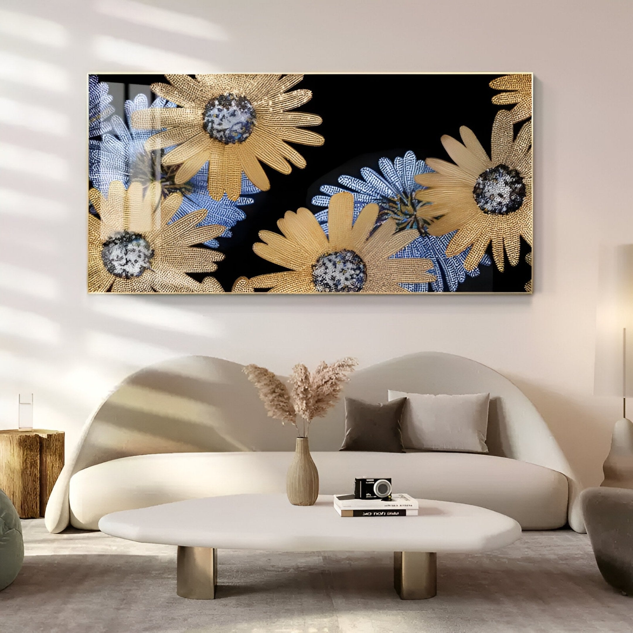 A modern living room with a curved white sofa, round coffee table, and dried flowers in a vase. Above the sofa hangs the Floravida Gold & Blue Crystal Daisy Floral 3D Wall Art by Giant Sculptures, featuring sparkling yellow and blue daisies.