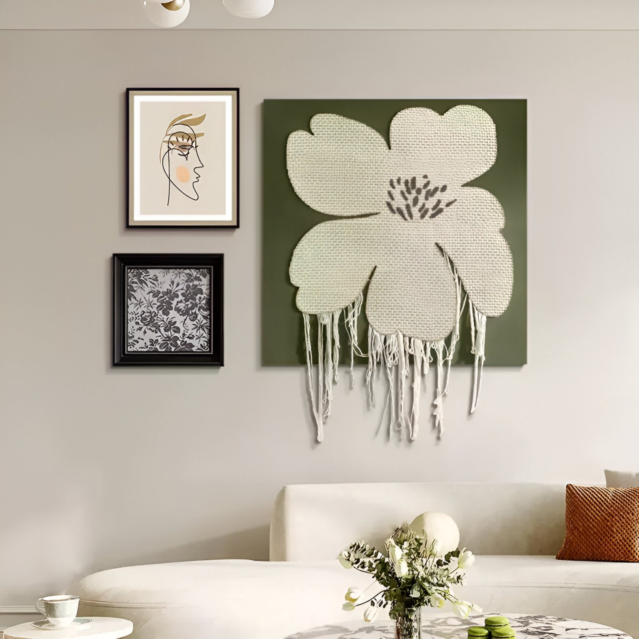 A modern living room with a beige sofa, round coffee table, and walls adorned with contemporary art, including the Florayne 3-Set Ivory Woven Textured 3D Wall Art by Giant Sculptures featuring abstract faces and textured floral designs with tassels.