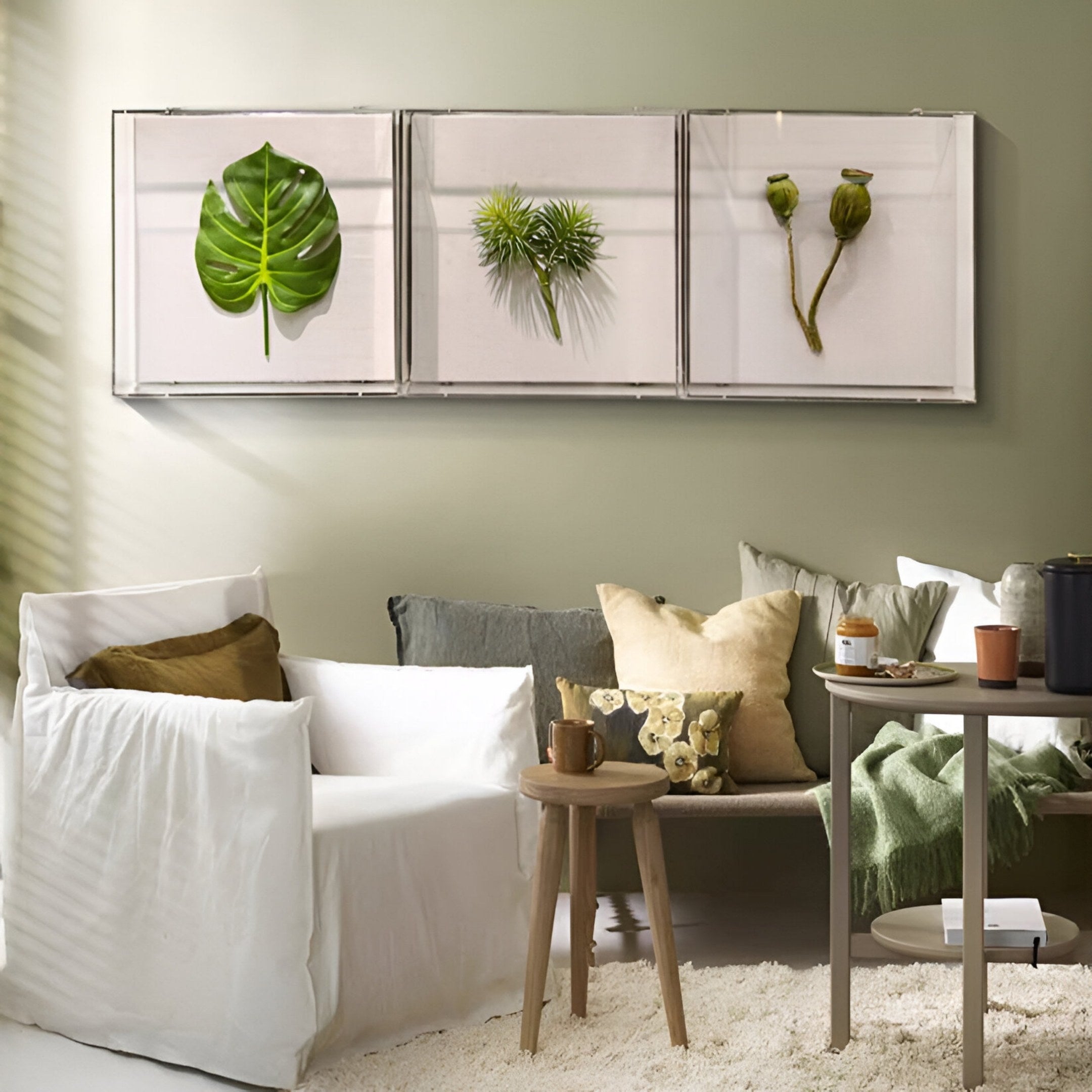 A cozy living room with neutral tones features a white armchair, side table, and Giant Sculptures’ Florvara Monstera Leaf Botanical 3-Panel Acrylic 3D Wall Art displayed above the sofa on a light green wall.