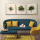 A modern living room with a blue sofa, yellow cushions, matching ottoman, yellow armchair, gold floor lamp, tea set tray, and Giant Sculptures Florvara Botanical Leaves 6-Panel Acrylic 3D Wall Art above. A yellow rug completes the look.