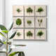 The Florvara Botanical Leaves 9-Panel Acrylic 3D Wall Art by Giant Sculptures features an array of green plant designs on a white wall, while a nearby potted rubber plant adds lush contrast to the bright, minimalist décor.