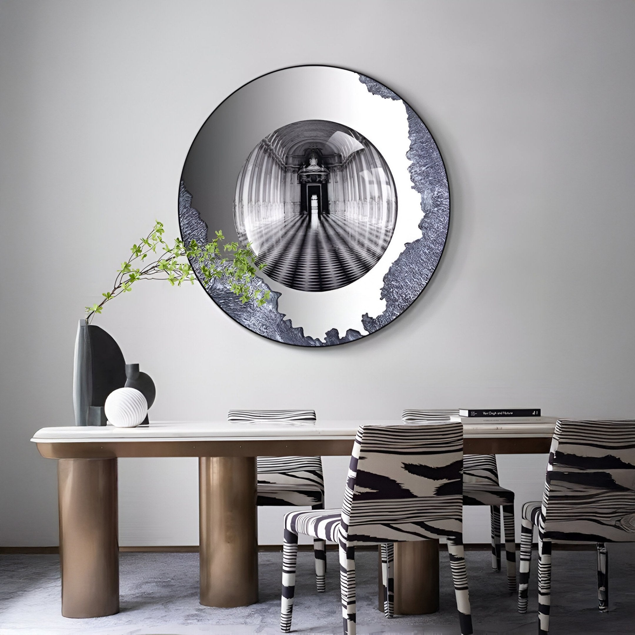 A modern dining room features the Portara Monochrome Hall Illusion Round 3D Wall Art by Giant Sculptures above the table, surrounded by zebra-patterned chairs. A black vase and a white object add to the minimalist, stylish atmosphere.