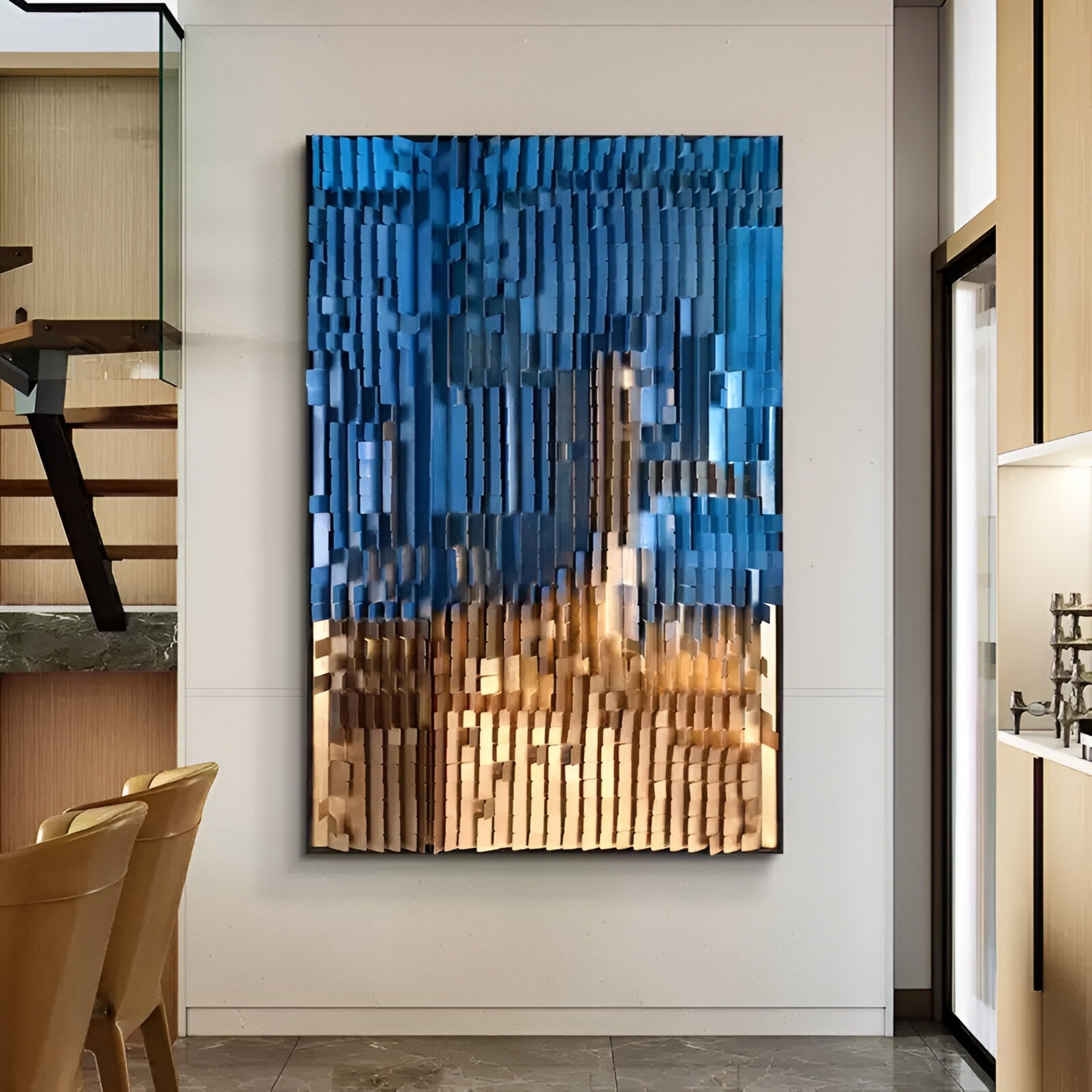 The Gradalis Blue & Gold Sculptural Metal 3D Wall Art by Giant Sculptures, featuring vertical ridges in blue and gold tones, is displayed on a white wall in a modern room with light wood furniture and a marble floor.