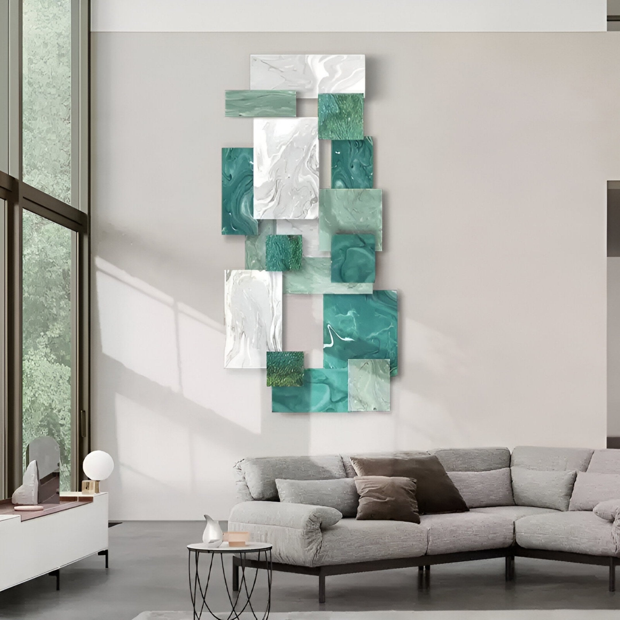 A modern living room with a gray sectional, light walls, large windows, and the Stravane II Green & White Mosaic Oil Canvas 3D Wall Art by Giant Sculptures—an abstract decor piece with green, white, and marble-textured geometric forms.