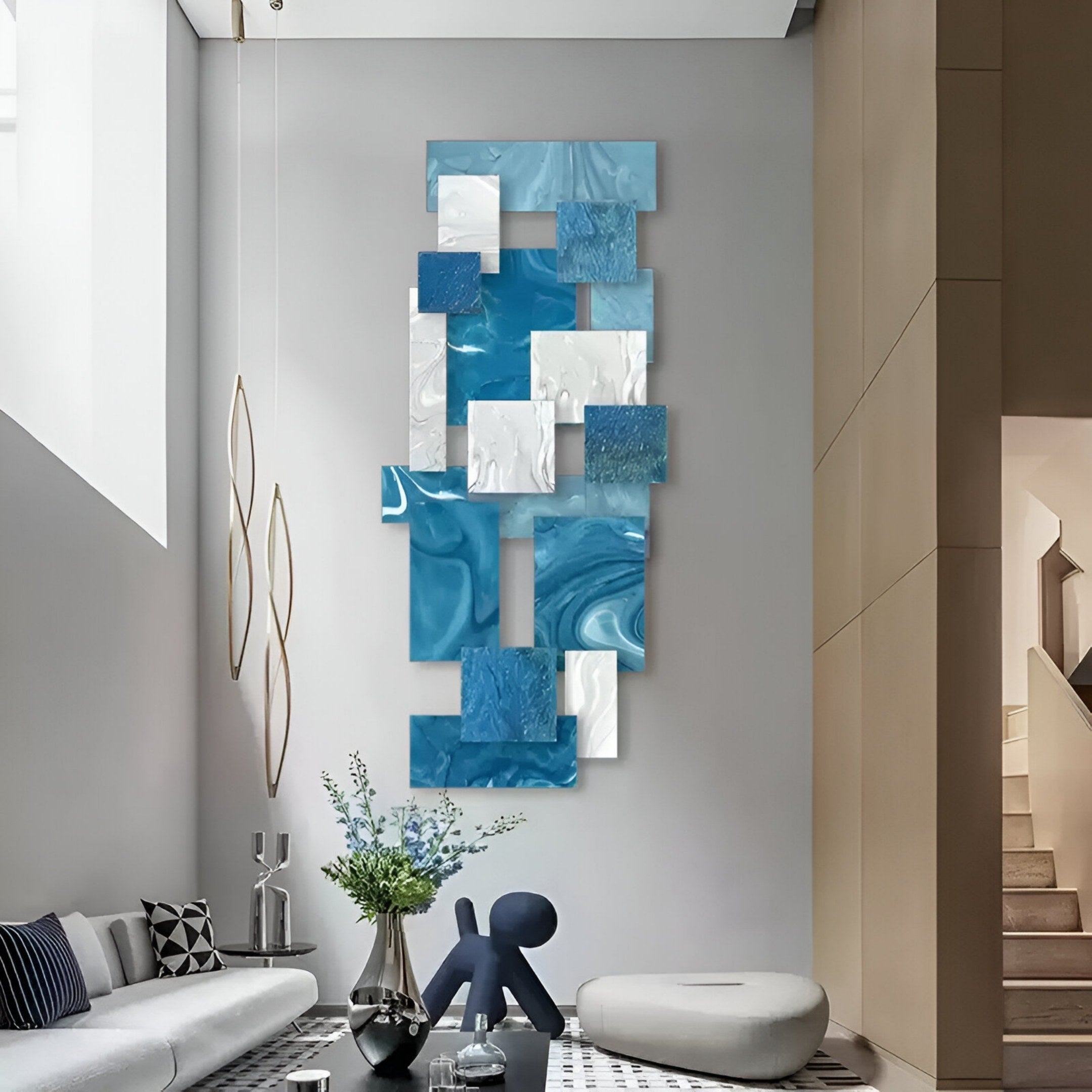 A modern living room showcases the Stravane Blue & White Mosaic Oil Canvas 3D Wall Art by Giant Sculptures, complemented by a sectional sofa, geometric table, pendant lights, and a visible staircase in the background.