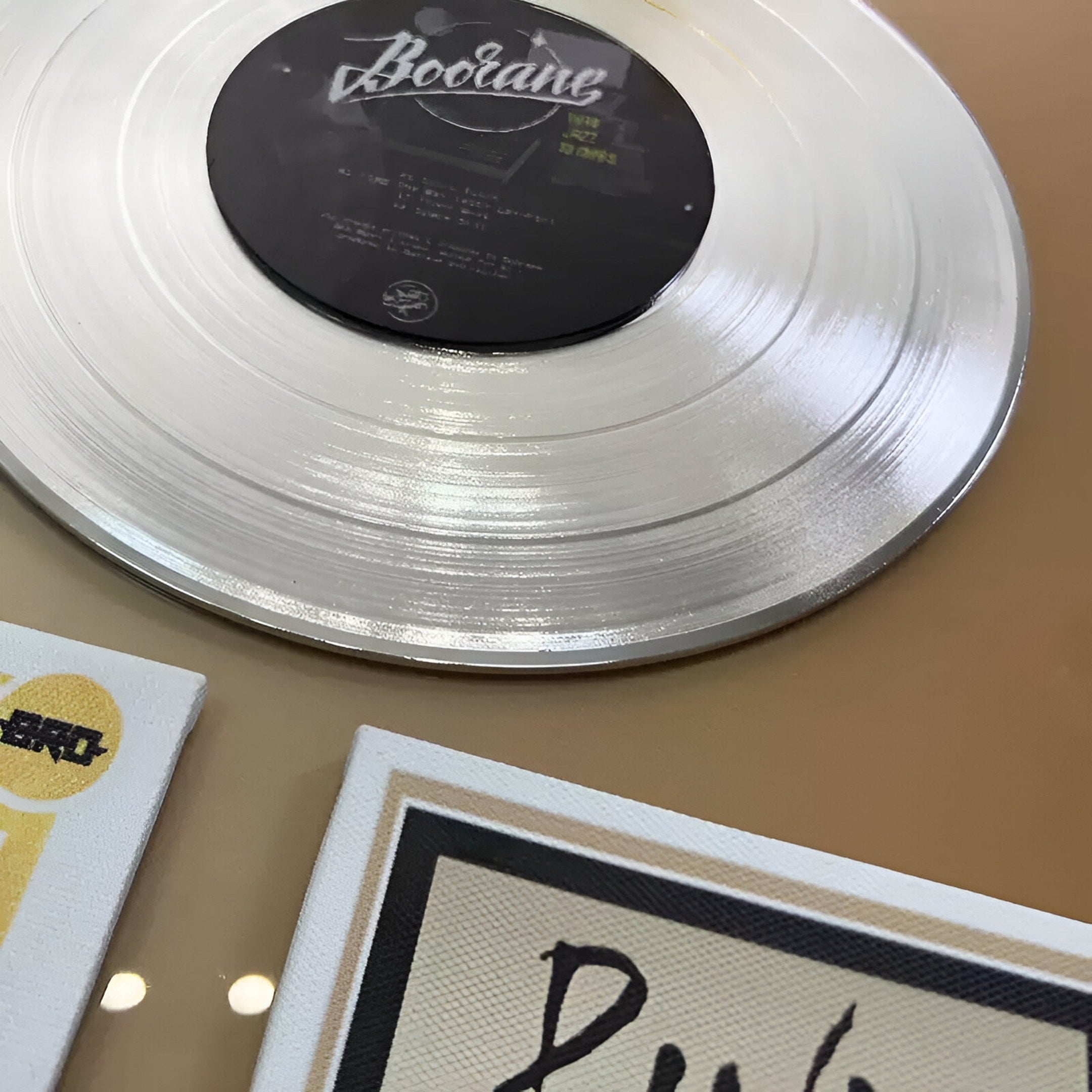 A close-up photo of the Sonarta Gold Multi-Panel Record & Silhouette Wall Art by Giant Sculptures, featuring a clear vinyl record on beige with modern accents—ideal for stylish music-themed décor or statement wall art.