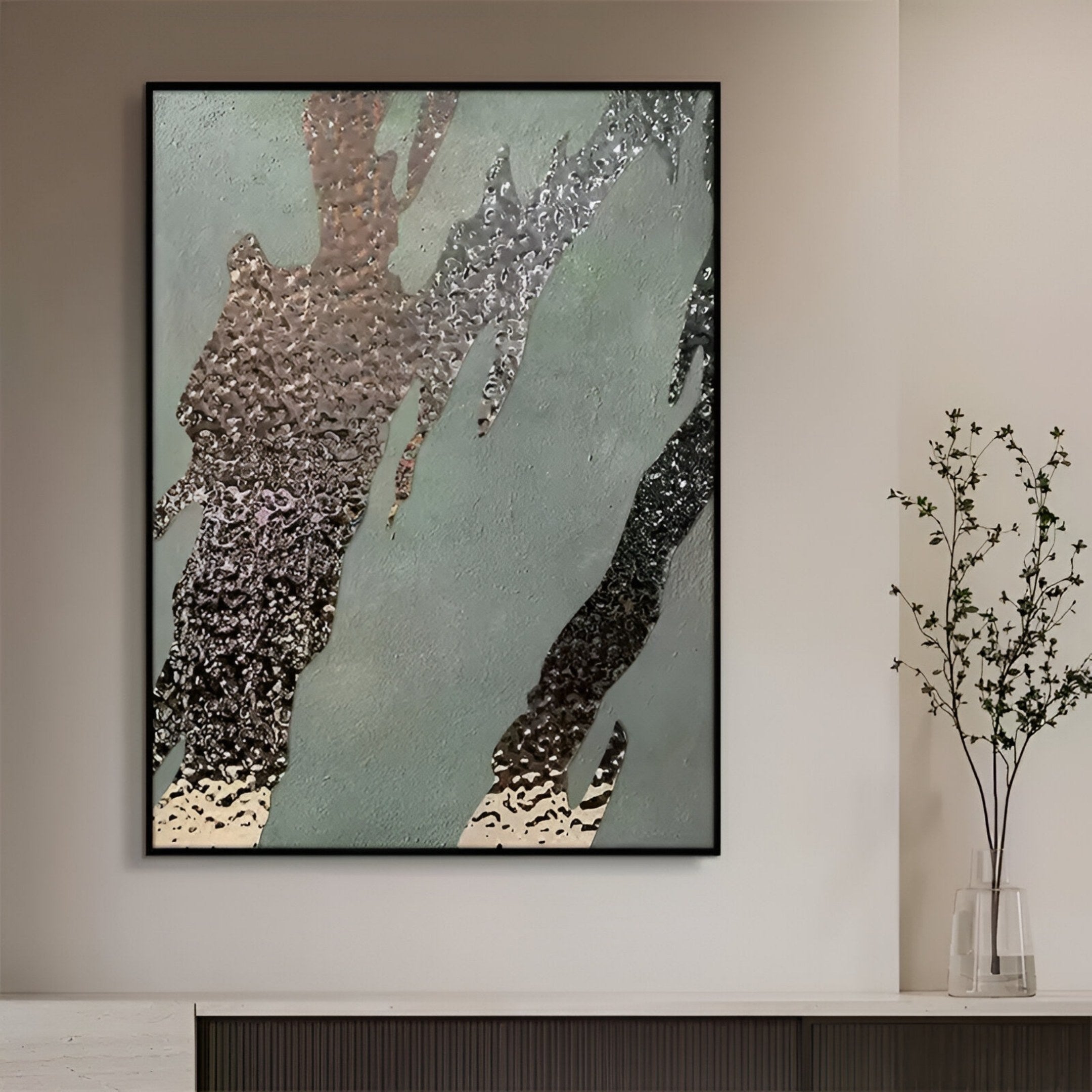 The Metallura Green & Silver Metallic Flow Abstract 3D Wall Art by Giant Sculptures, featuring wavy silver, gray, and green textures, hangs on a beige wall above a dark cabinet beside a slender vase with delicate branches.