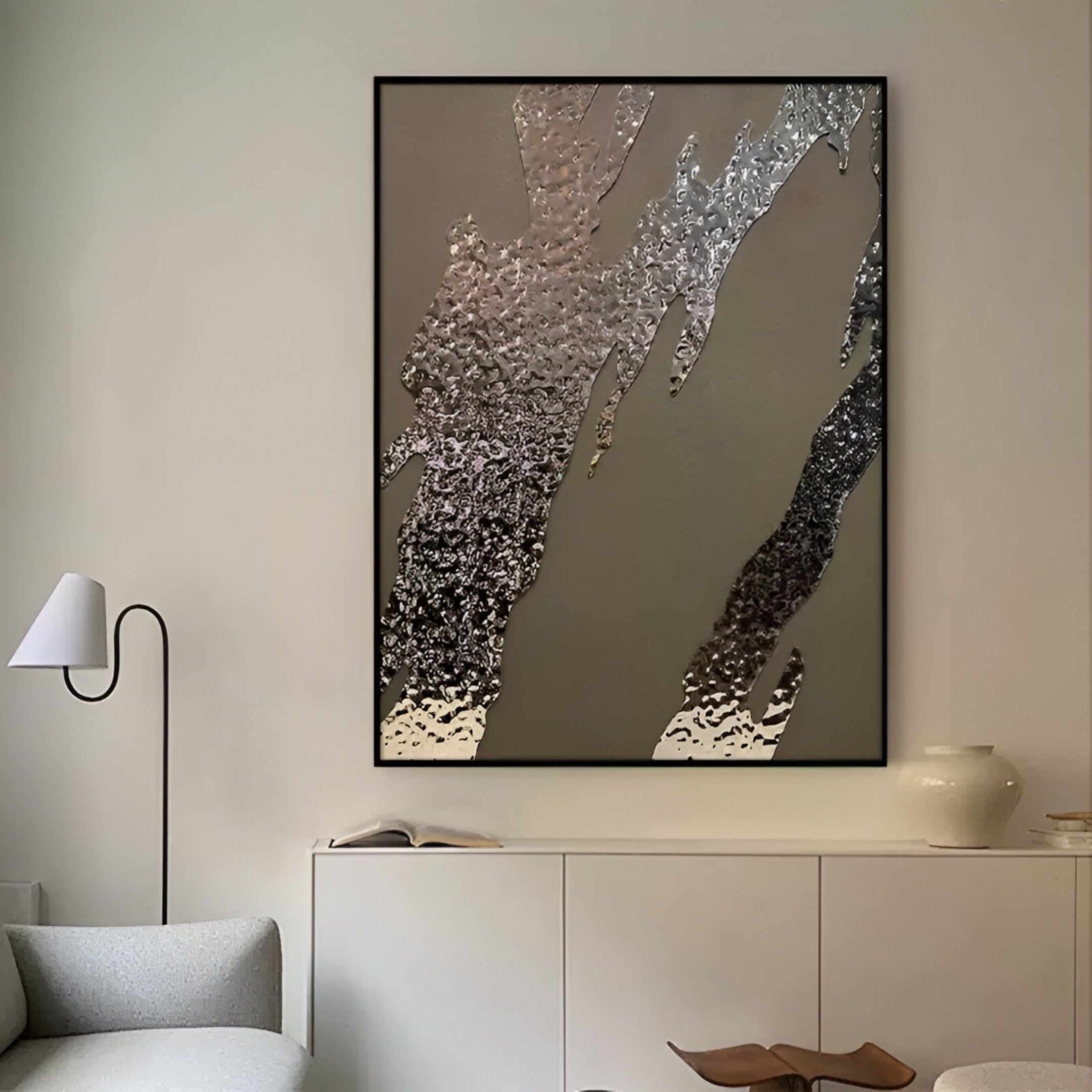 A modern living room with a light grey sofa, minimalist white lamp, and white sideboard features the Metallura Bronze Metallic Flow Abstract 3D Wall Art by Giant Sculptures above, accented by a white vase and wooden decor.