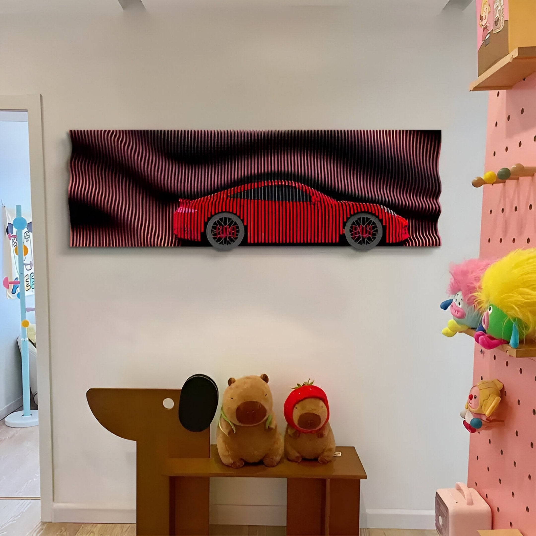 The Velocedra Red Sportscar 3D Relief Wall Art by Giant Sculptures hangs on a white wall above two plush toys on a wooden bench in a colorful room, with shelves of toys on the right.