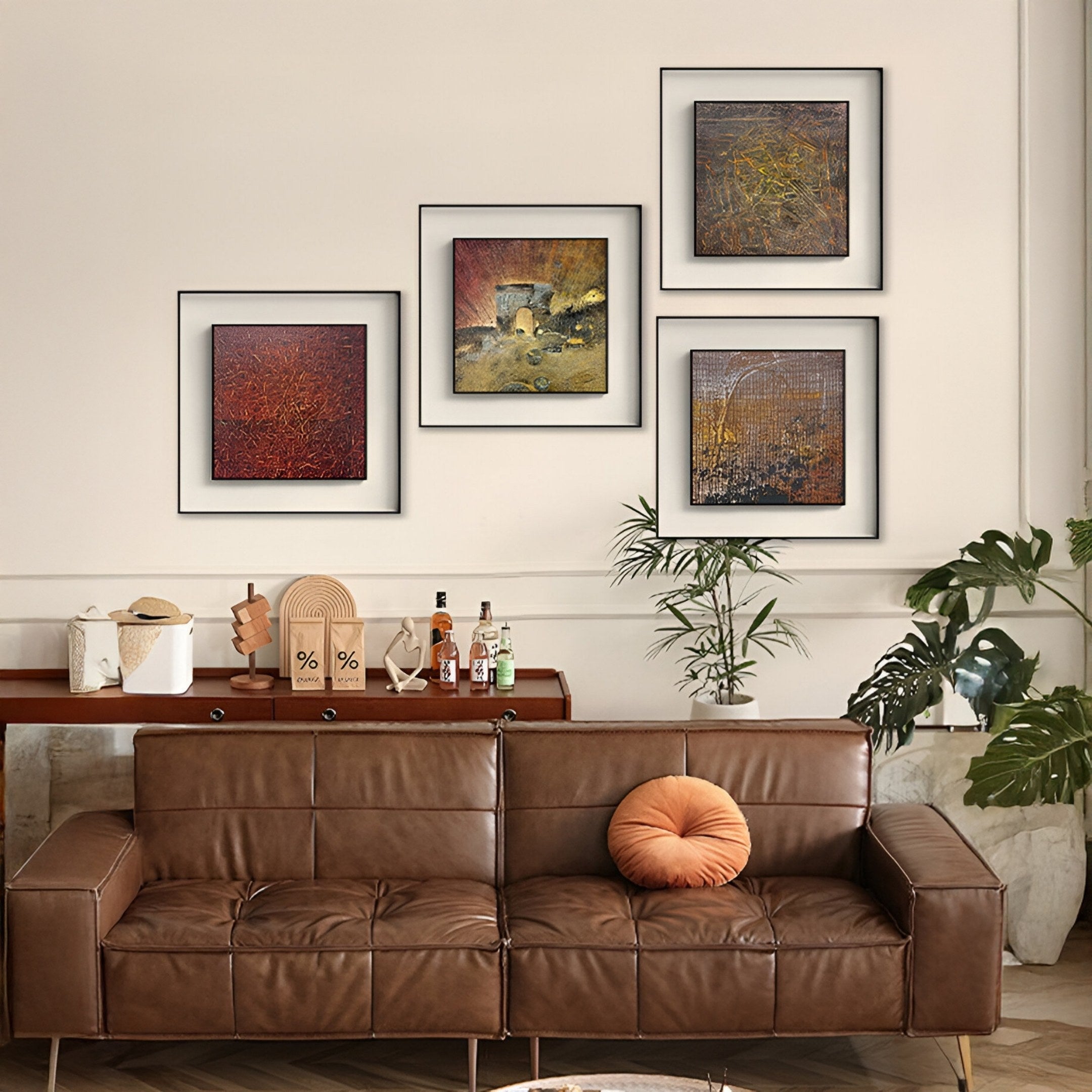 A modern living room with a brown leather sofa, an orange round pillow, a bar on a wooden console, lush plants, and four Fiorenze Burnished Geometric Fragment Square 3D Wall Art pieces by Giant Sculptures on a cream wall.