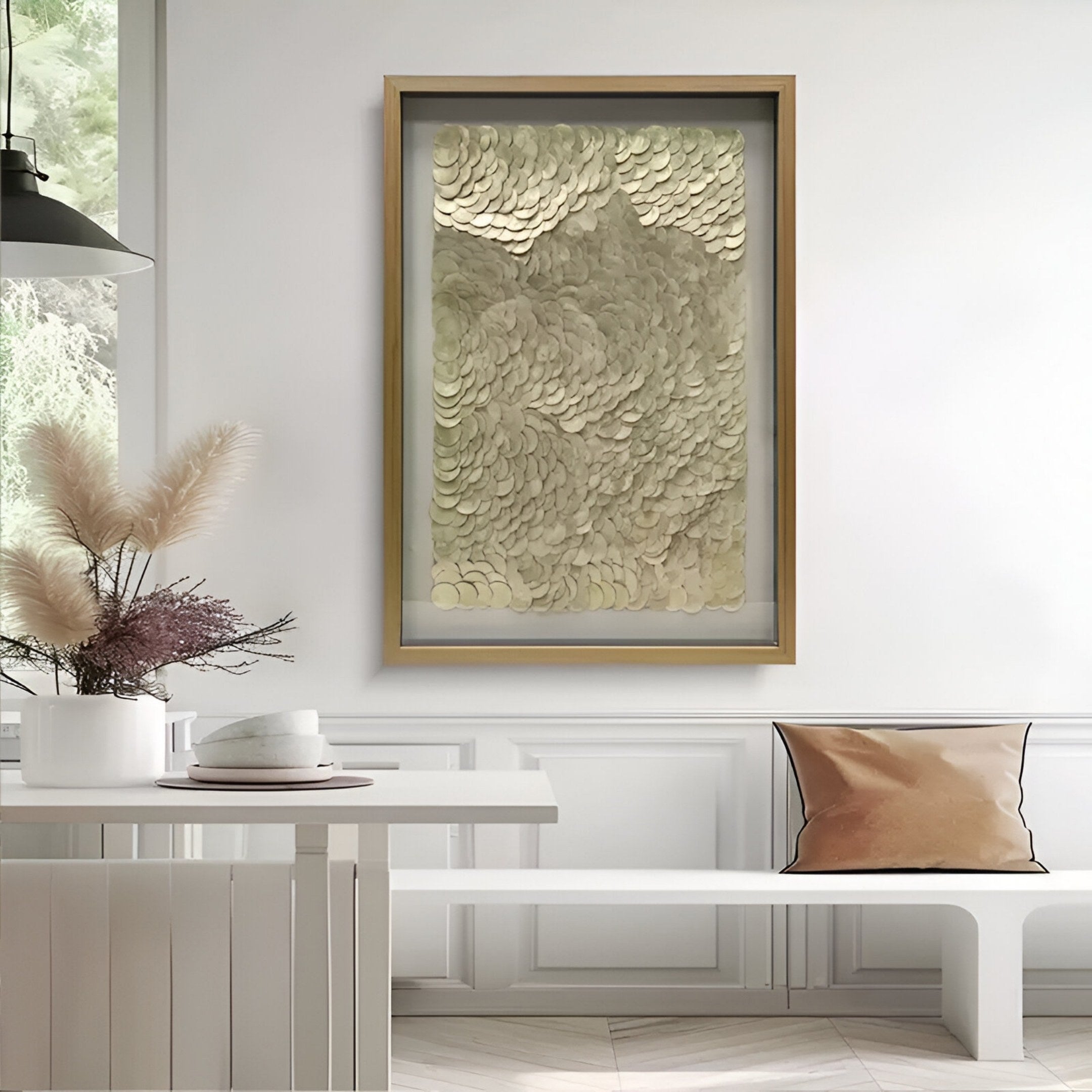 A modern, minimal living space featuring a white bench and table, tan and cream throw pillow, vase with dried pampas grass, and Giant Sculptures’ Orraya Golden Shell Disc Layered Framed 3D Wall Art for an elevated touch.