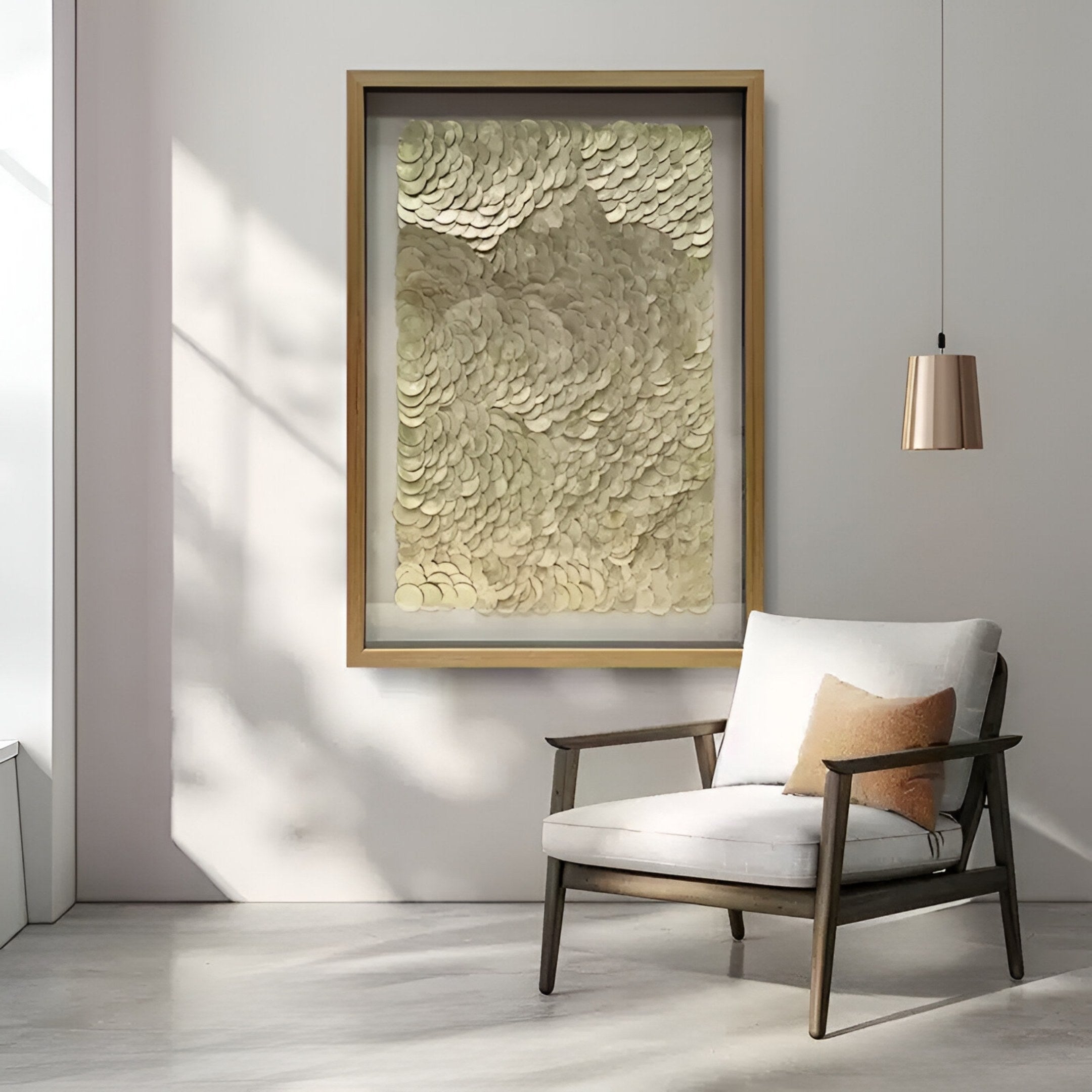 A modern, minimalist room features a wooden armchair with beige cushion, a copper pendant lamp, and the Orraya Golden Shell Disc Layered Framed 3D Wall Art by Giant Sculptures. Sunlight creates soft shadows on light walls and floor.