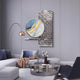 A modern living room with gray walls, Giant Sculptures’ Aurivista Blue & Silver Abstract Circle Panel 3D Metal Wall Art, abstract art, a round metallic coffee table, white sectional with pillows, beige throw, gold-shade floor lamp, and dark accent chair.