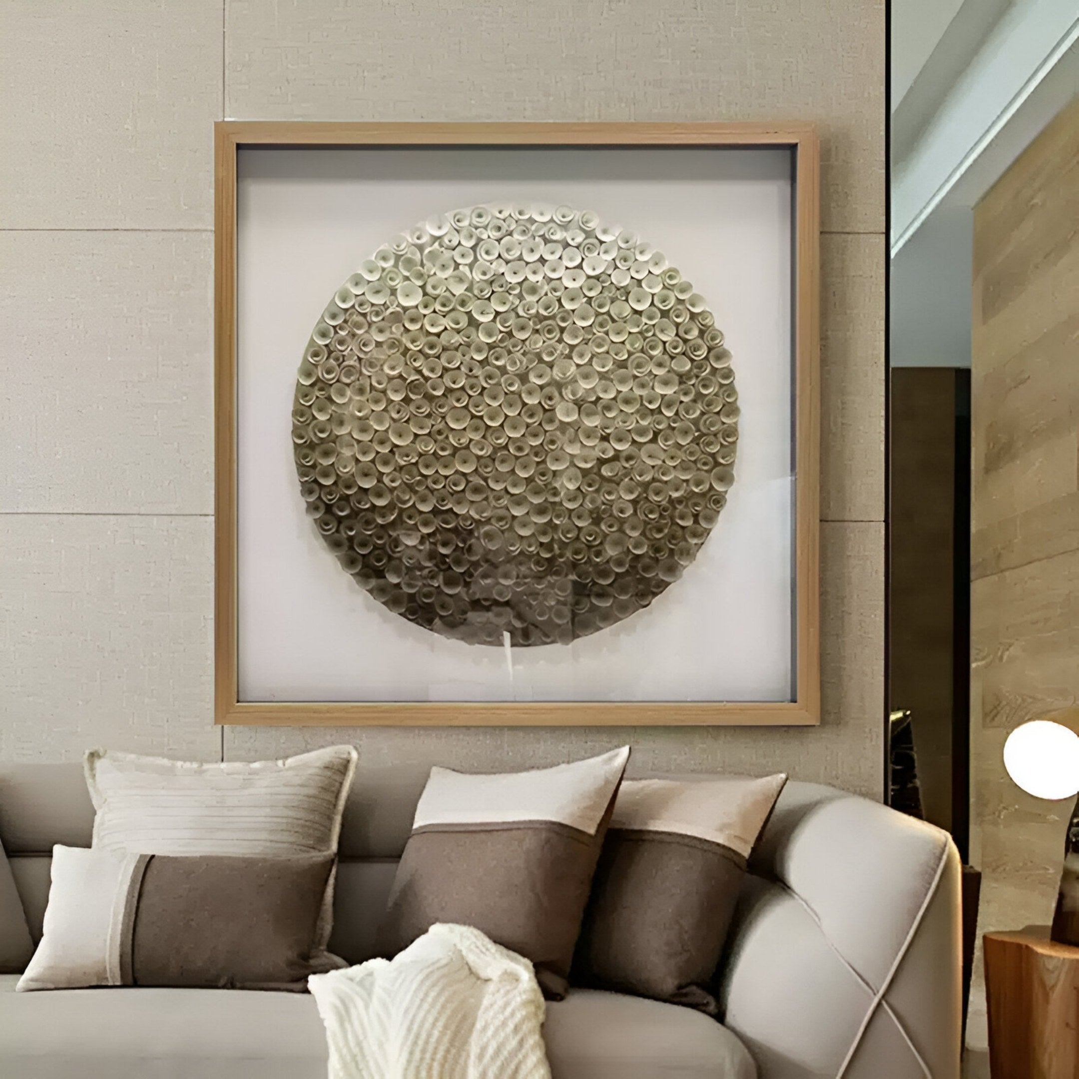 The Aureliare Pearl Gold Rolled Floral Framed 3D Wall Art by Giant Sculptures hangs above a beige couch, showcasing metallic discs. Beige and brown pillows and a textured blanket add to the modern living room décor.
