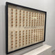 The Fortuna Mahjong Carved Wood Tile Linen Wall Art shown at an angle on a pale wall, the raised wooden tiles catching light and casting shadows across the linen ground.